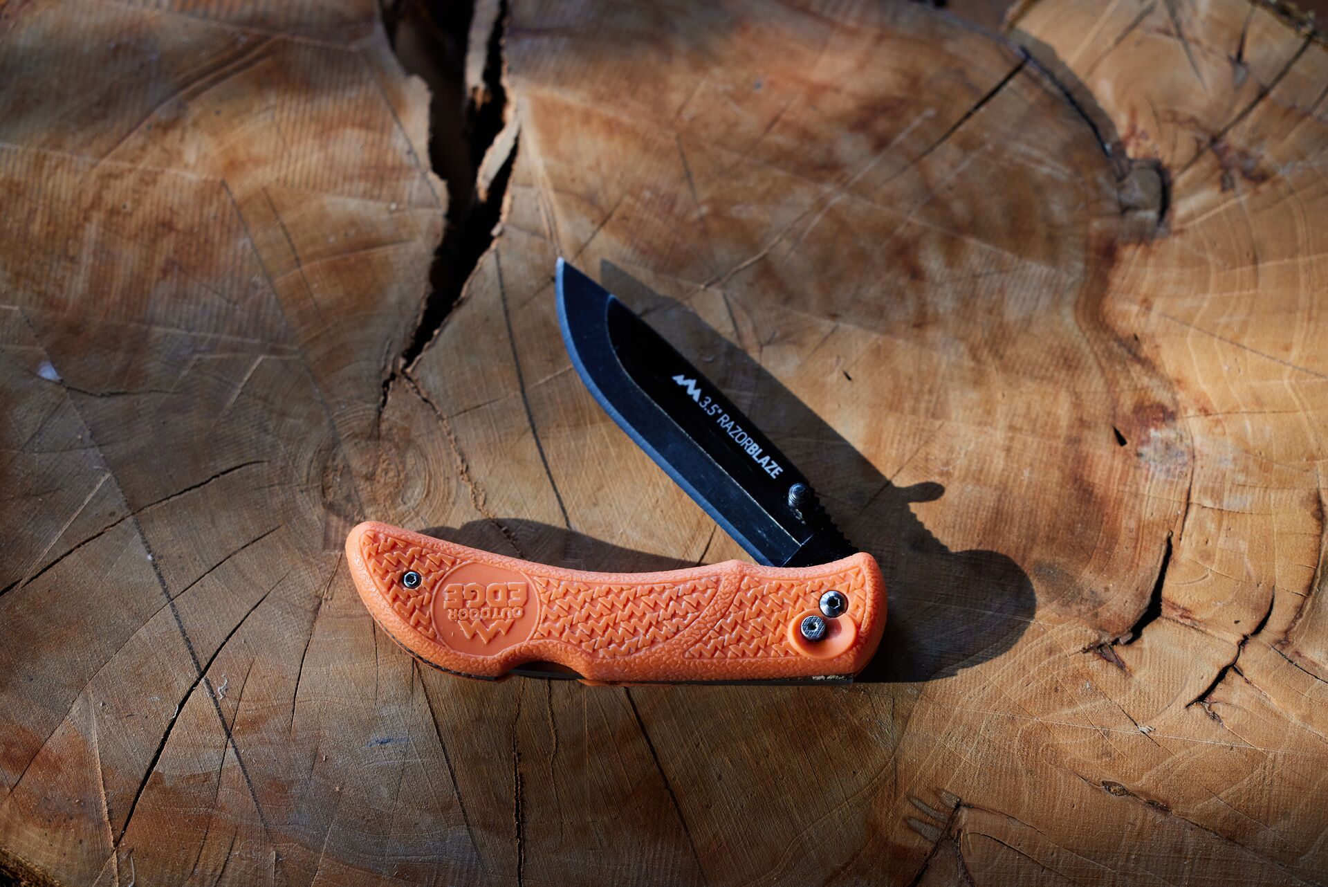 A folding knife sits on a wood stump, choosing hunting knives concept. 