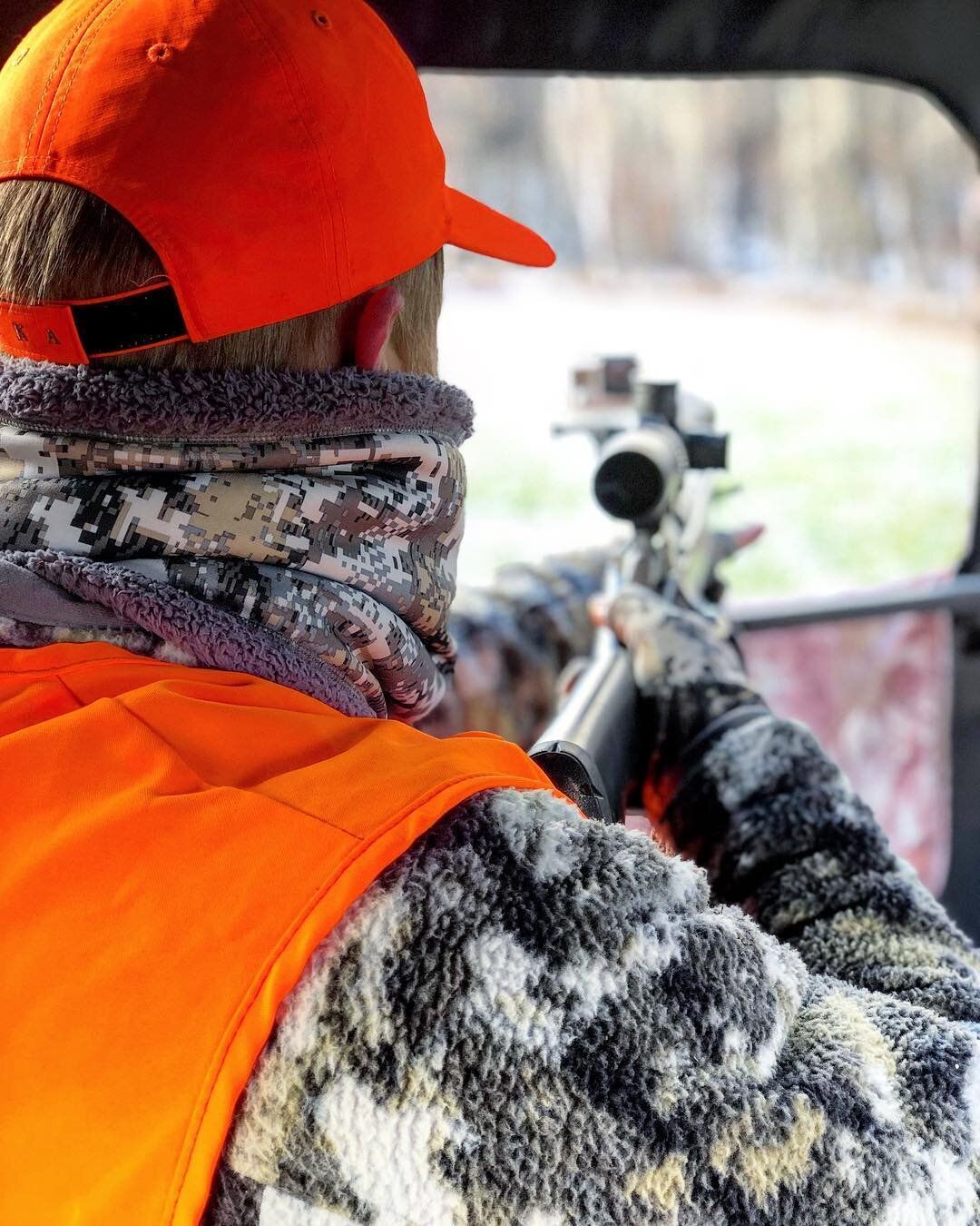 A hunter with a rifle and scope on hunting land. 