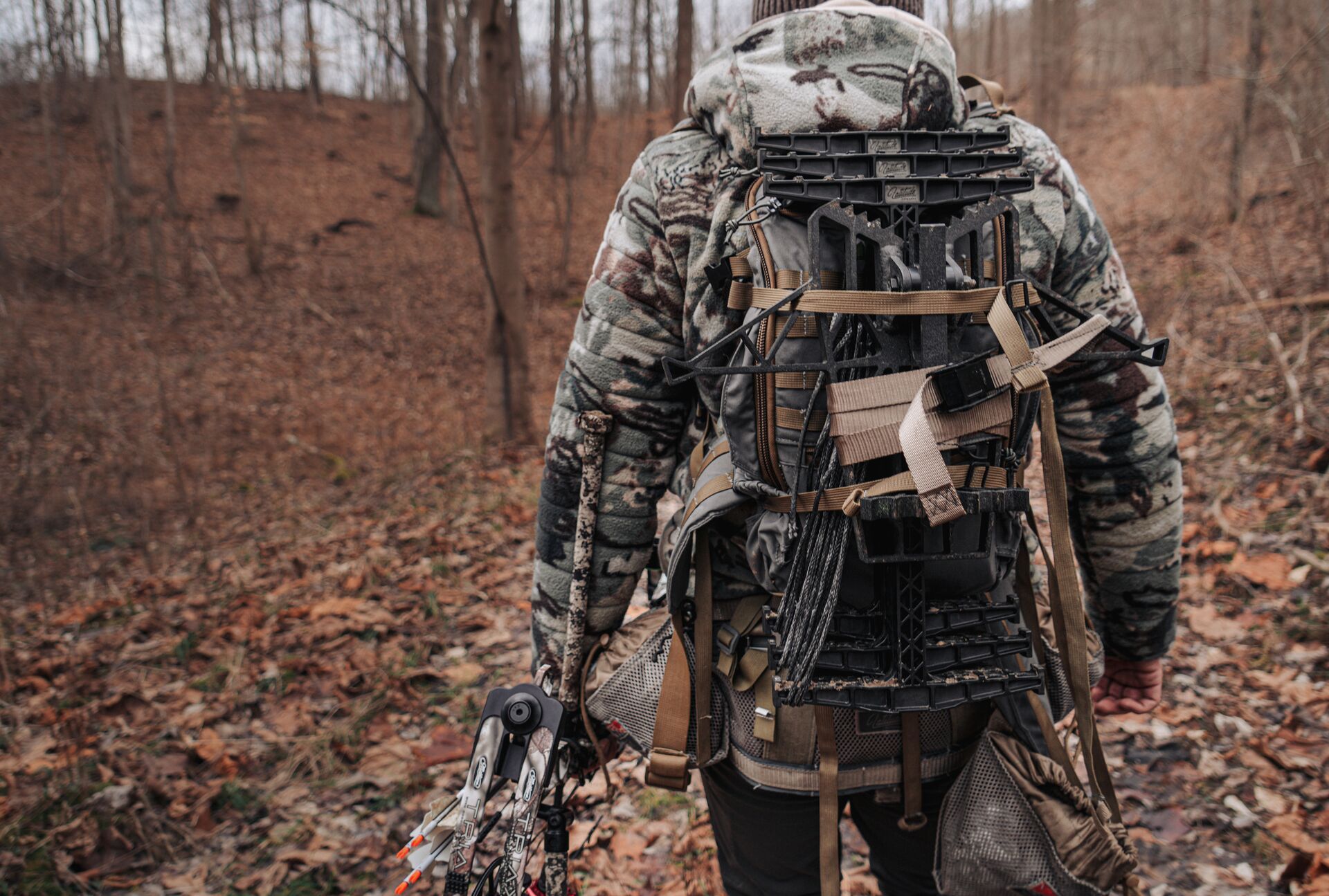 A hunter in camo carries a bow through the woods, deer hunting with a bow concept. 