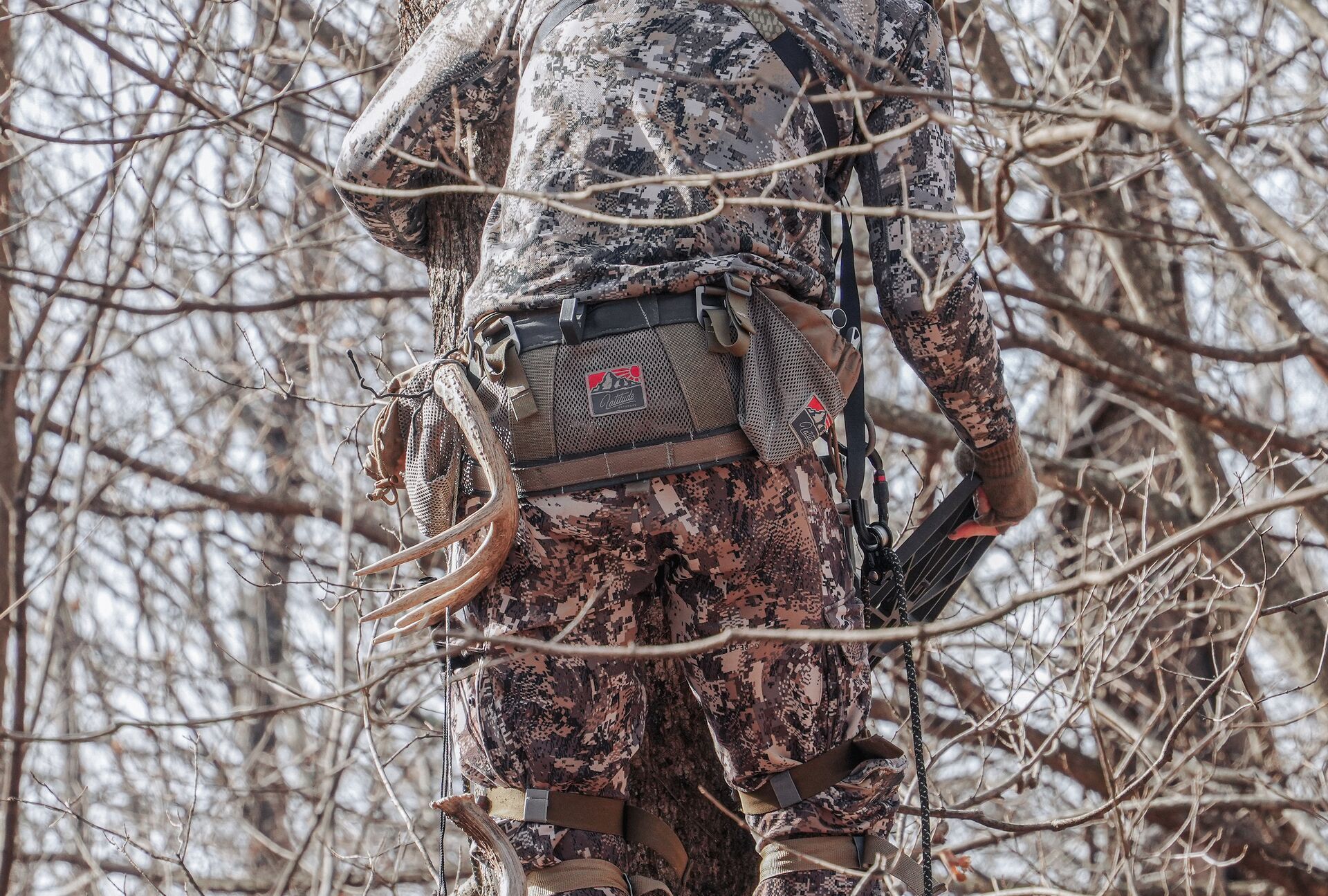 A hunter in camo setting in a tree for saddle hunting. 