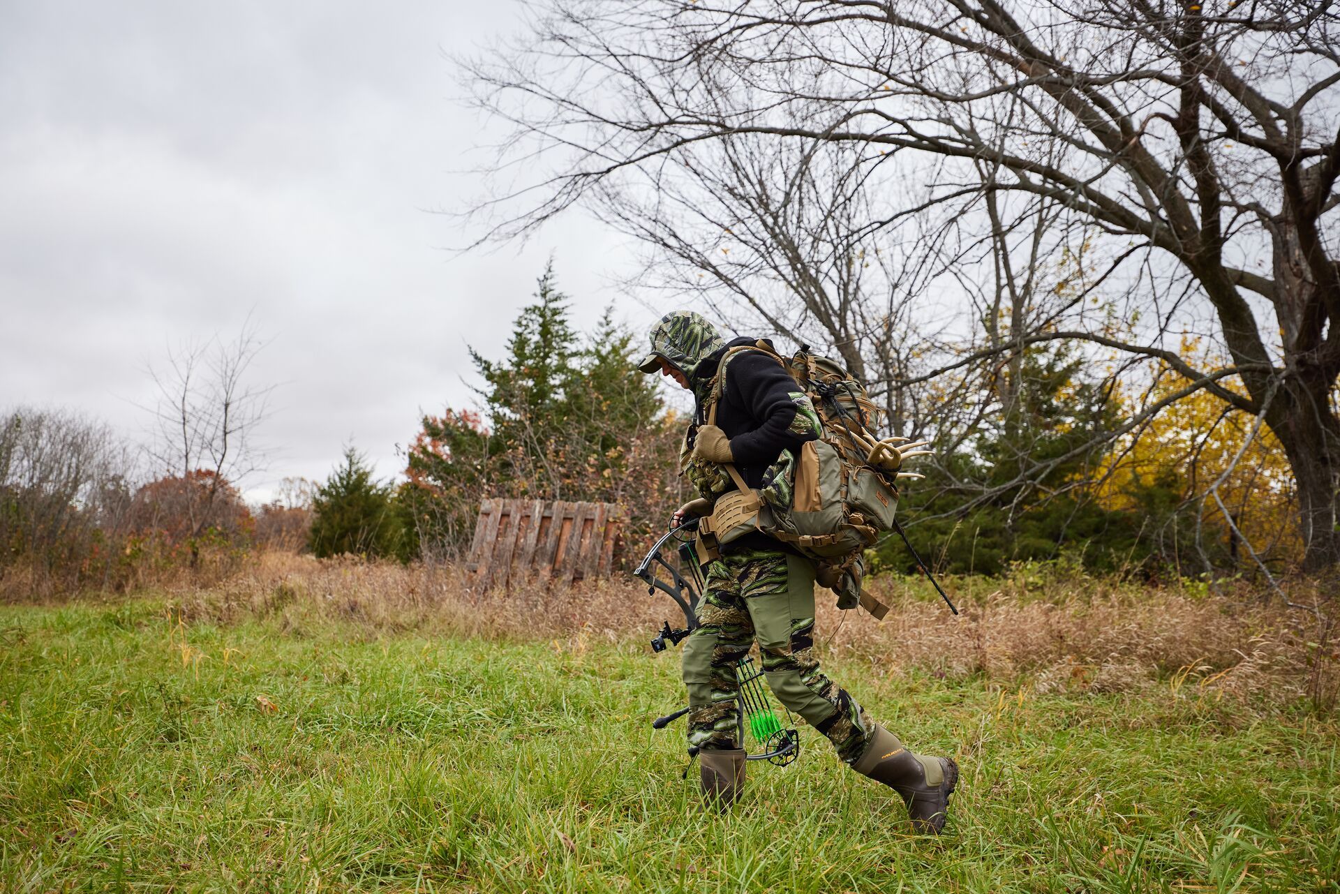 Hunter John Dudley walks through a field with a bow and gear.