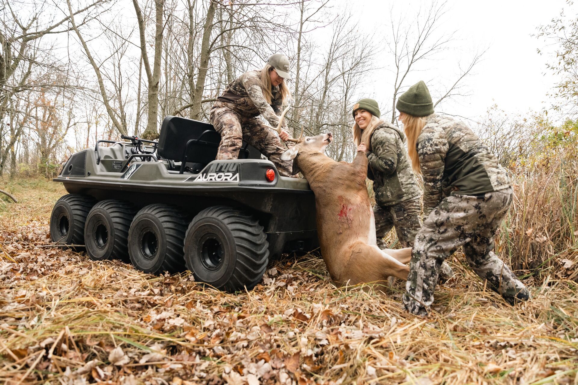 Three female hunters load a buck onto a tractor after a hunt. 