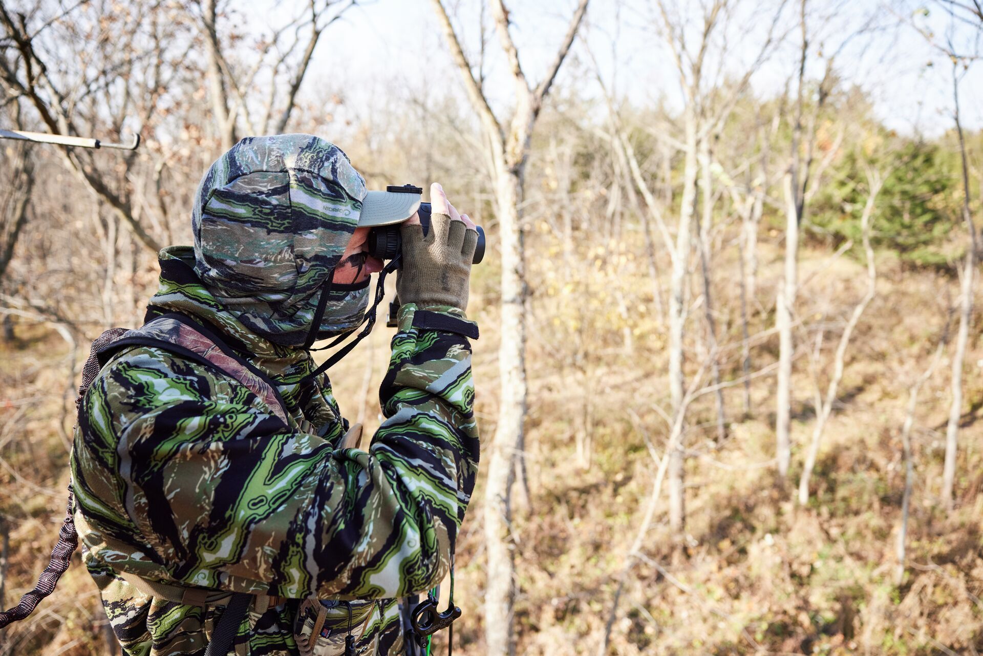 Hunter in camo in the woods uses binoculars. 