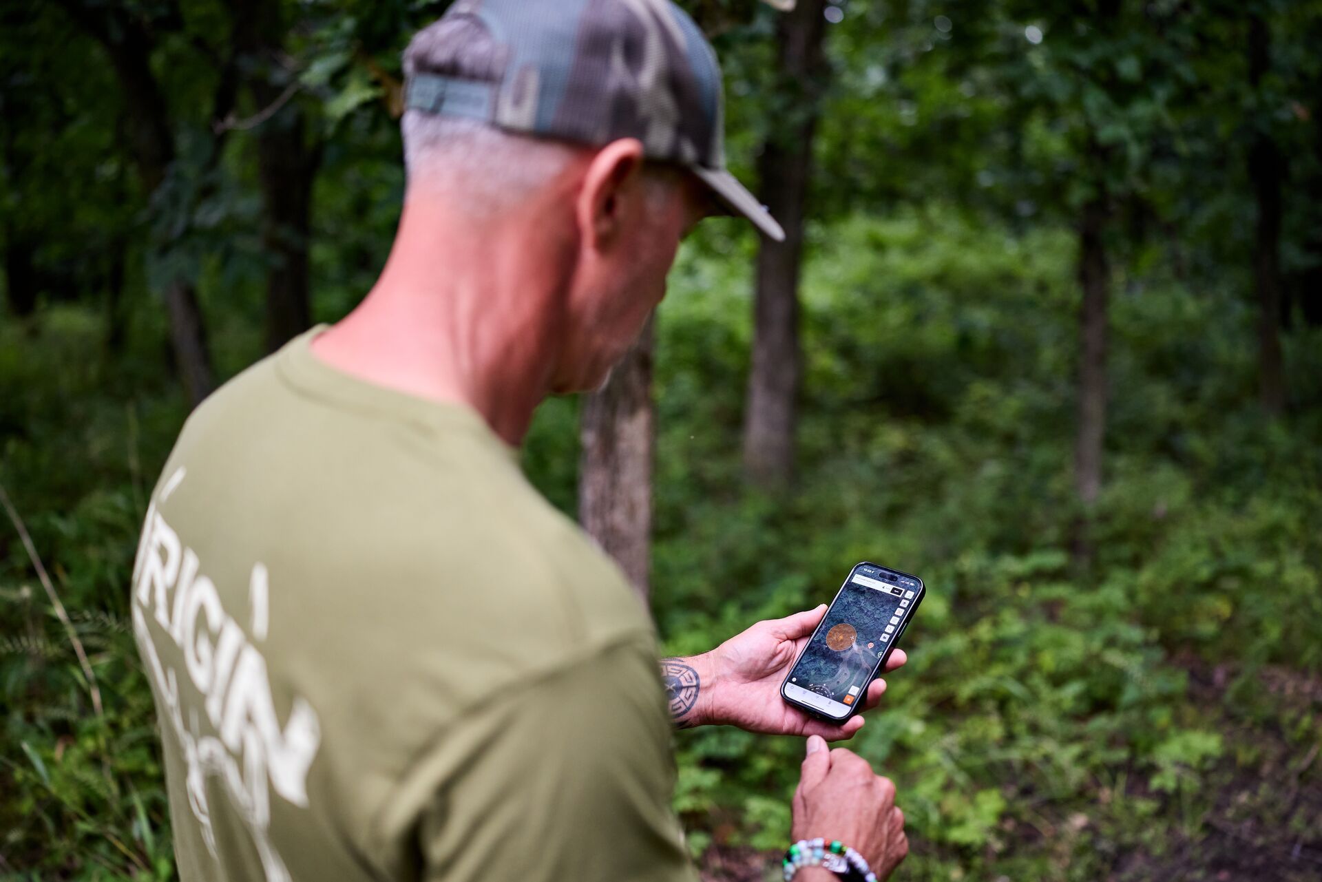 Hunter John Dudley in the woods with a phone showing the HuntWise hunting app. 