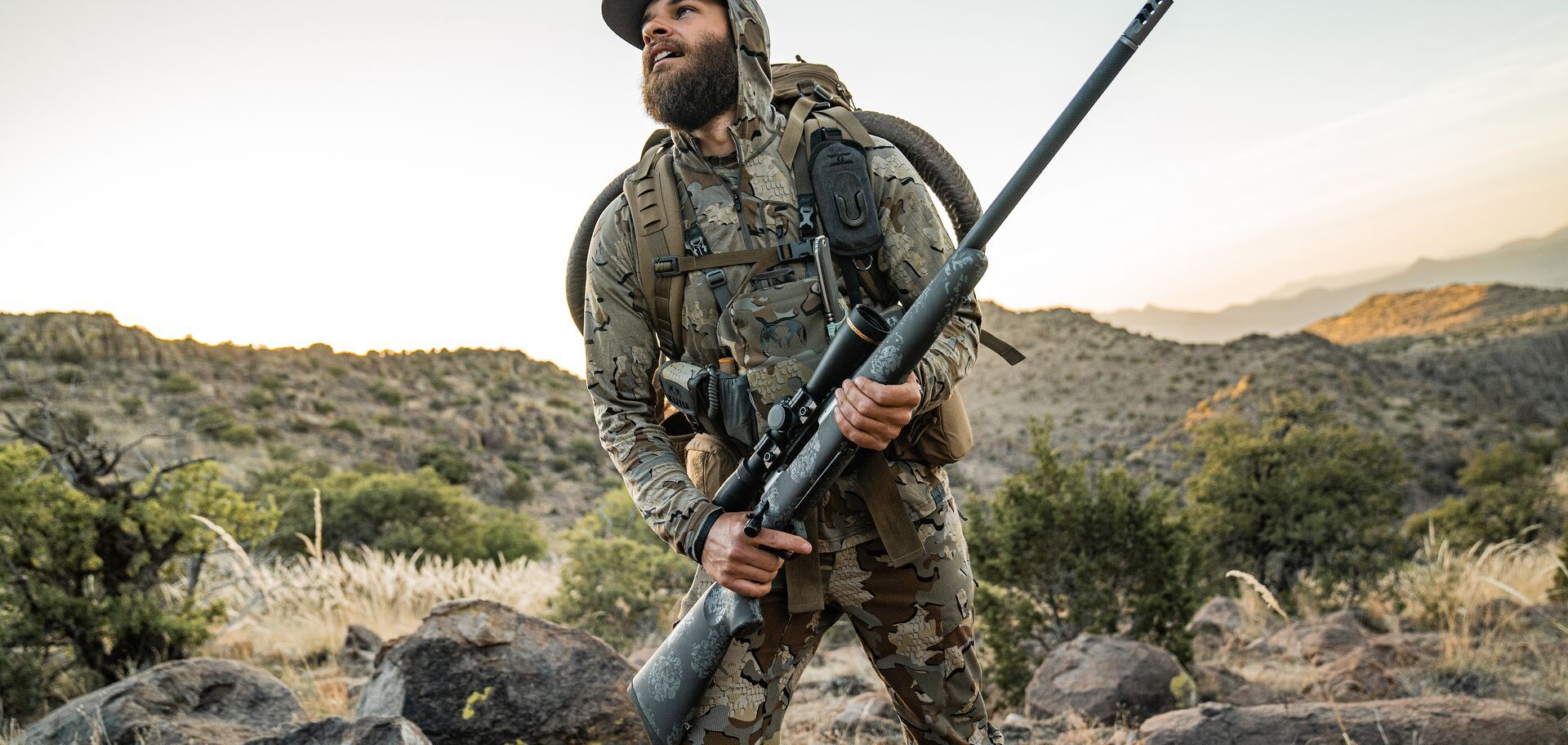 Hunter in camo on rocky ground with bolt action rifle, 