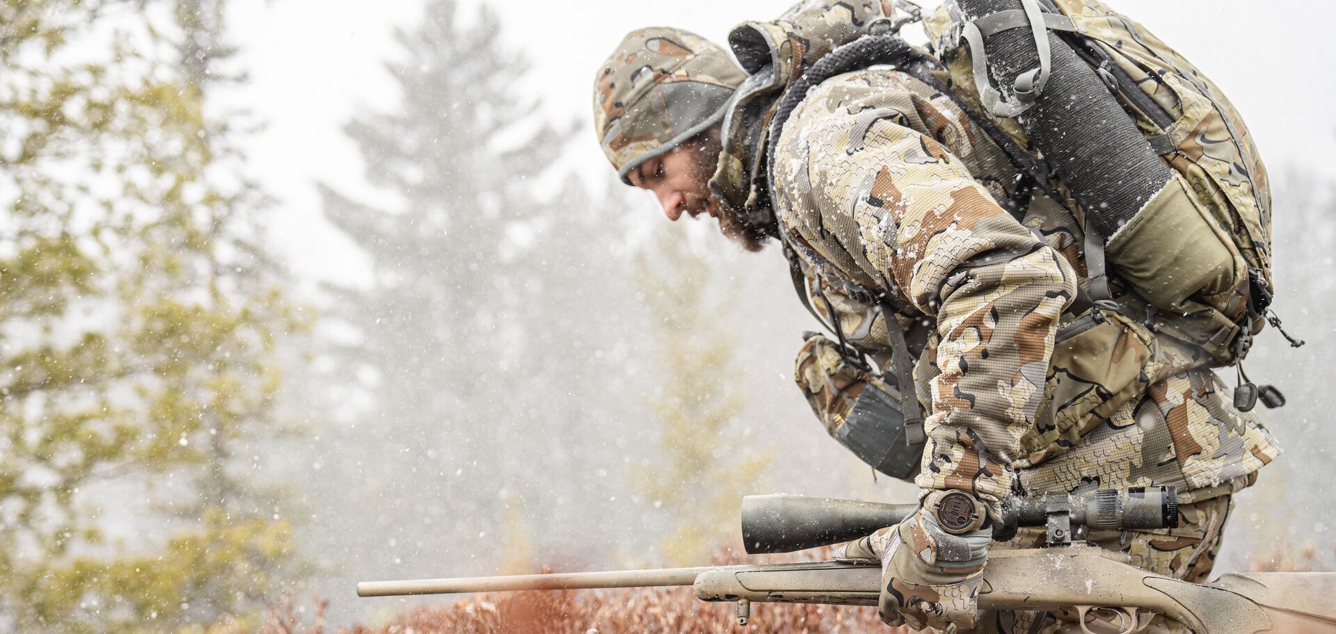 Hunter in camo with rifle walks in light snow, December hunting tips concept. 