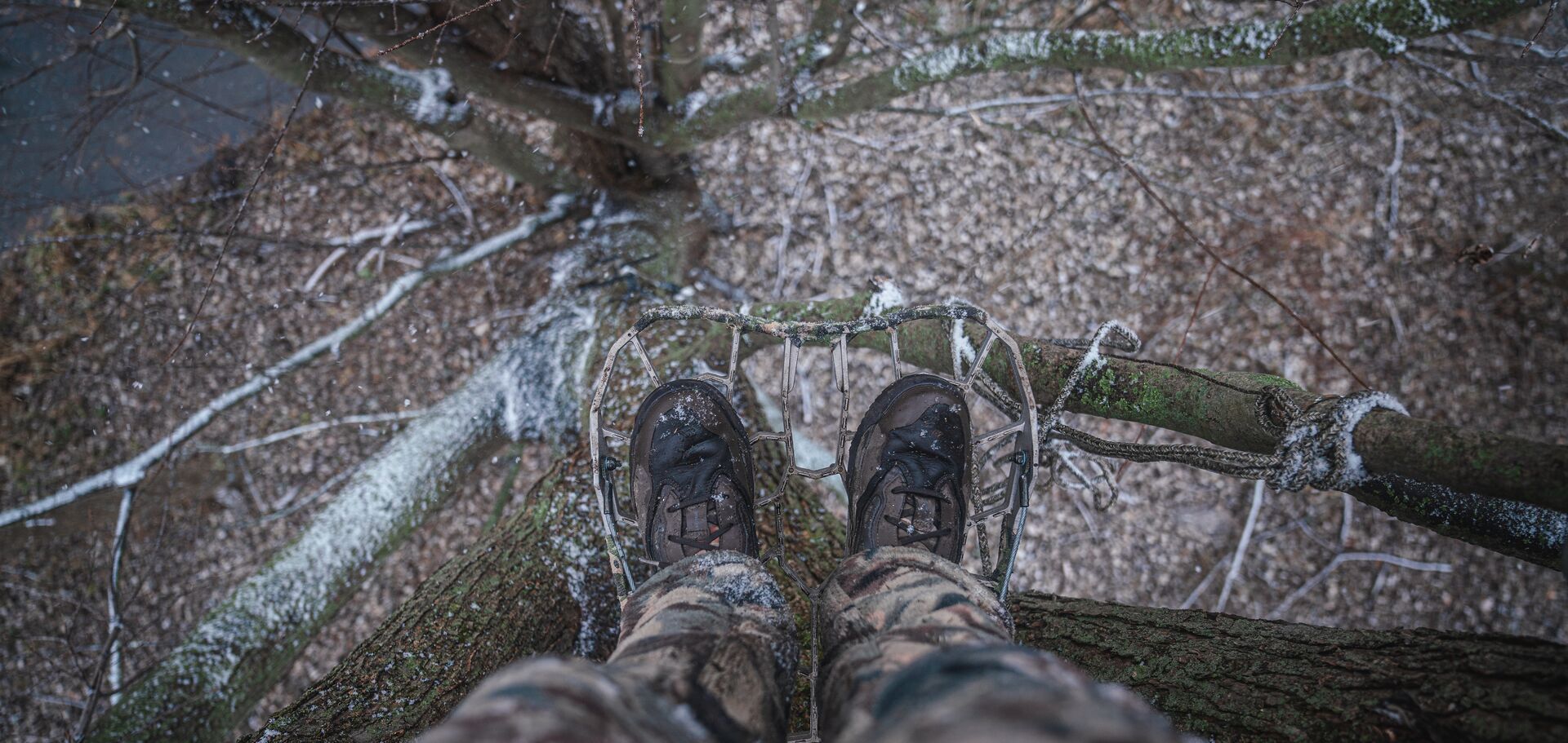 Looking down at feet in tree platform with light snow around. 