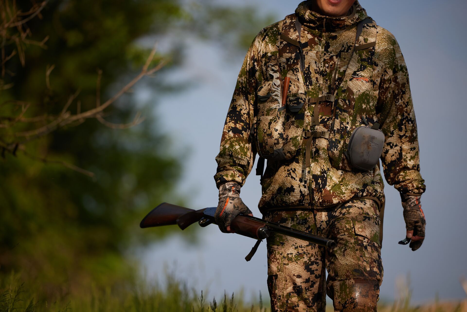 Hunter in turkey camo with shotgun walks through field. 