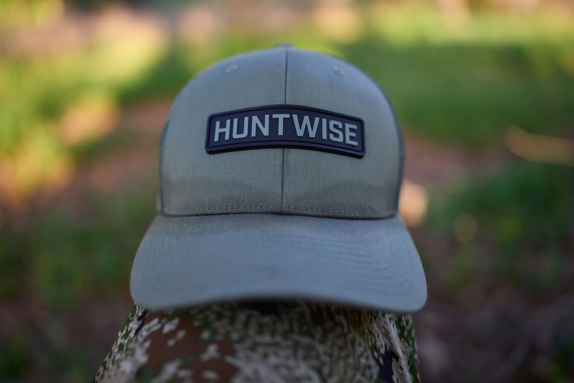 A HuntWise hat on someone's knee in the woods.