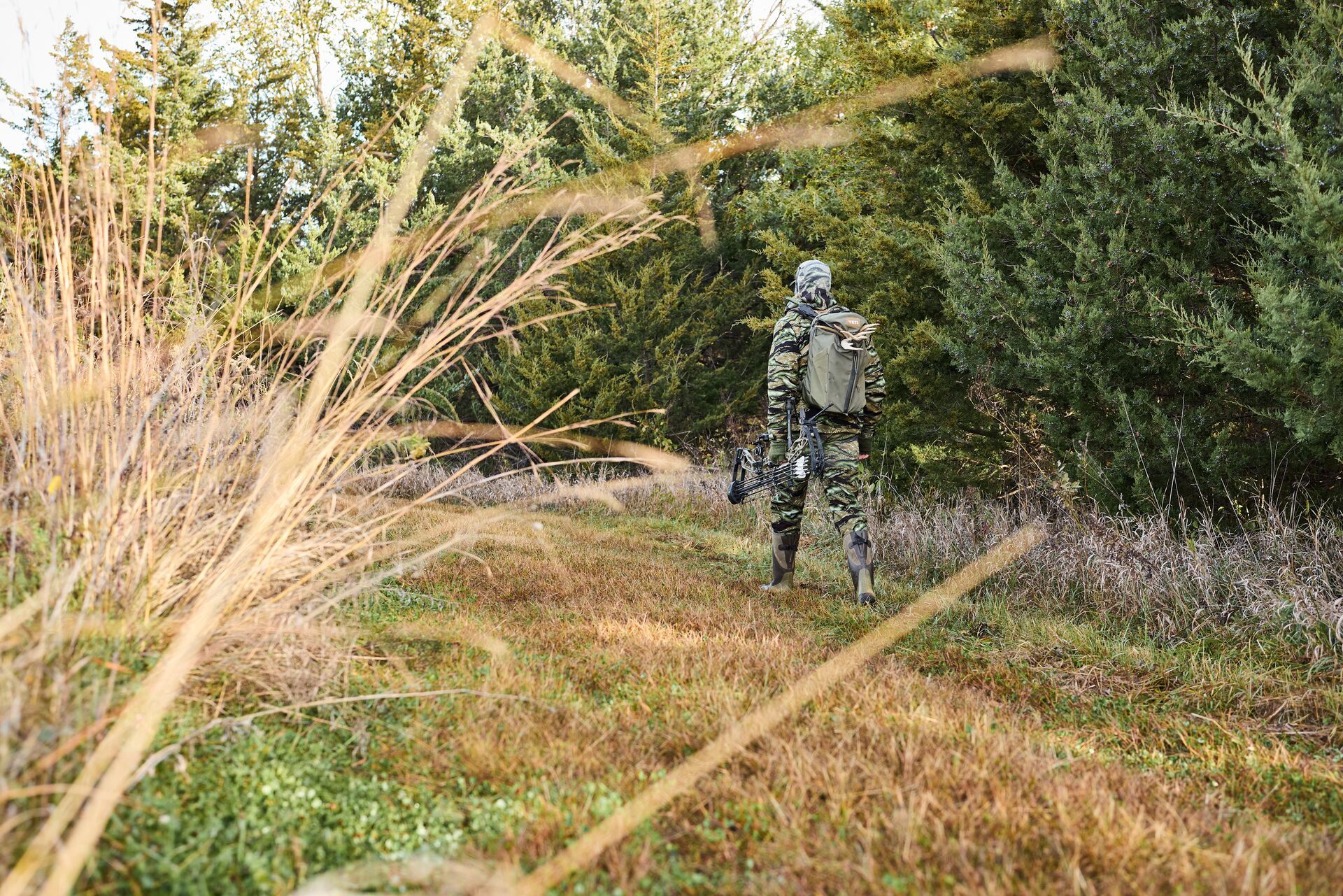 A hunter with gear and bow walks on hunting land. 