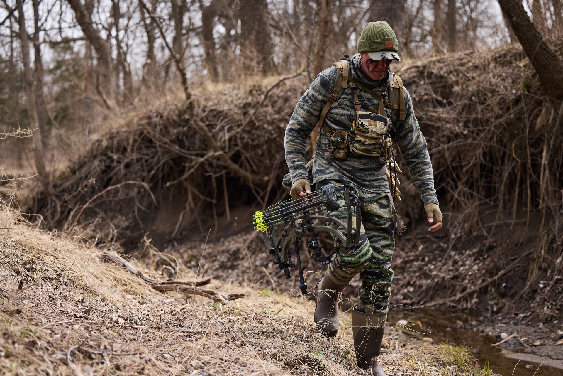 HuntWise Pro and hunter John Dudley walks through brush with gear, bow hunting fitness concept.