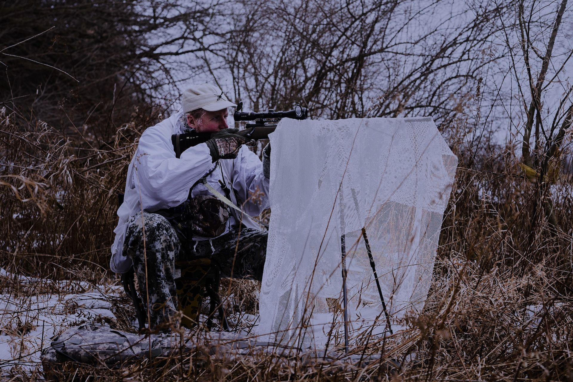 A hunter with a rifle, scope, and gear for a coyote hunt at night. 