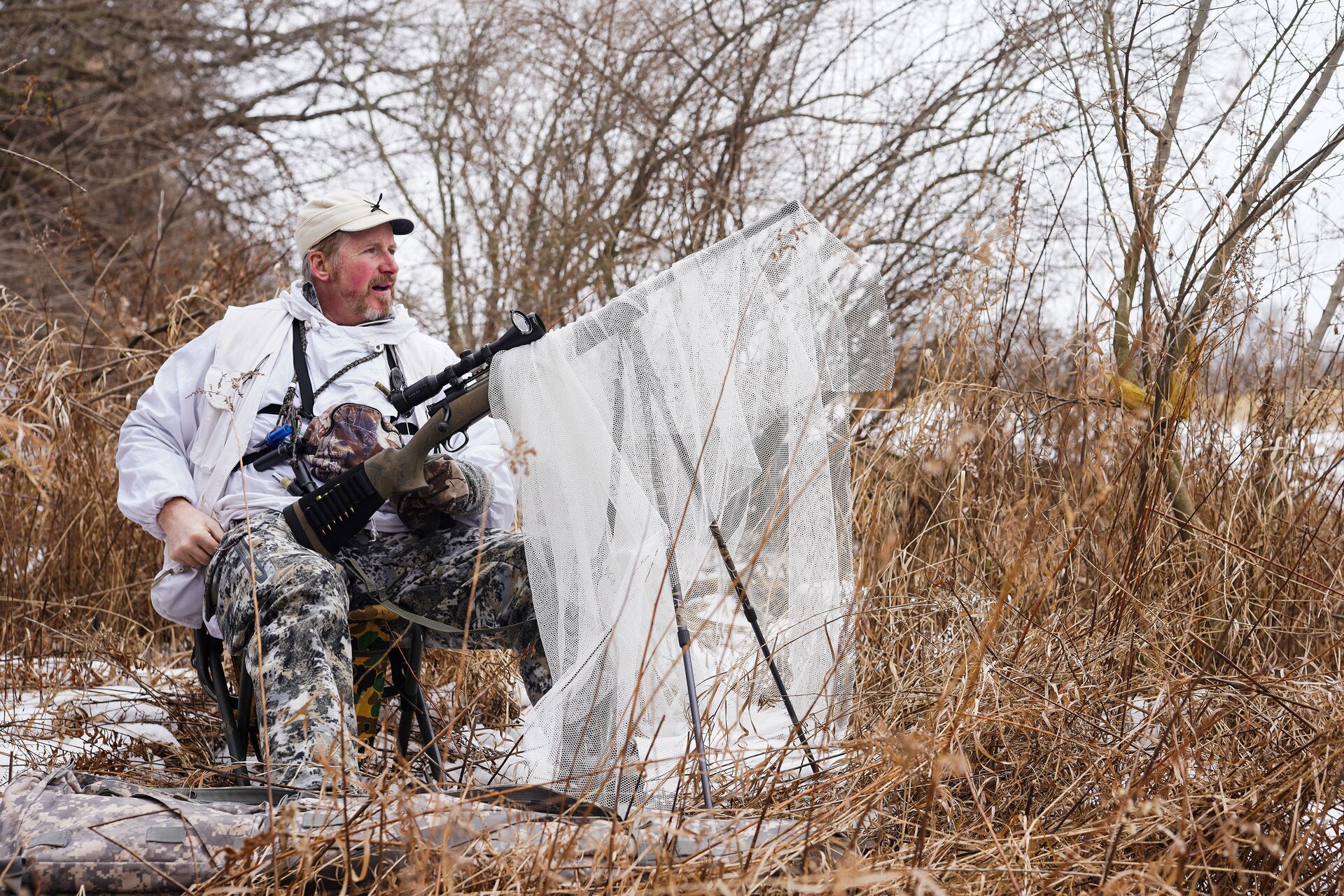 A hunter sits on a stool and uses a stand for coyote hunting. 