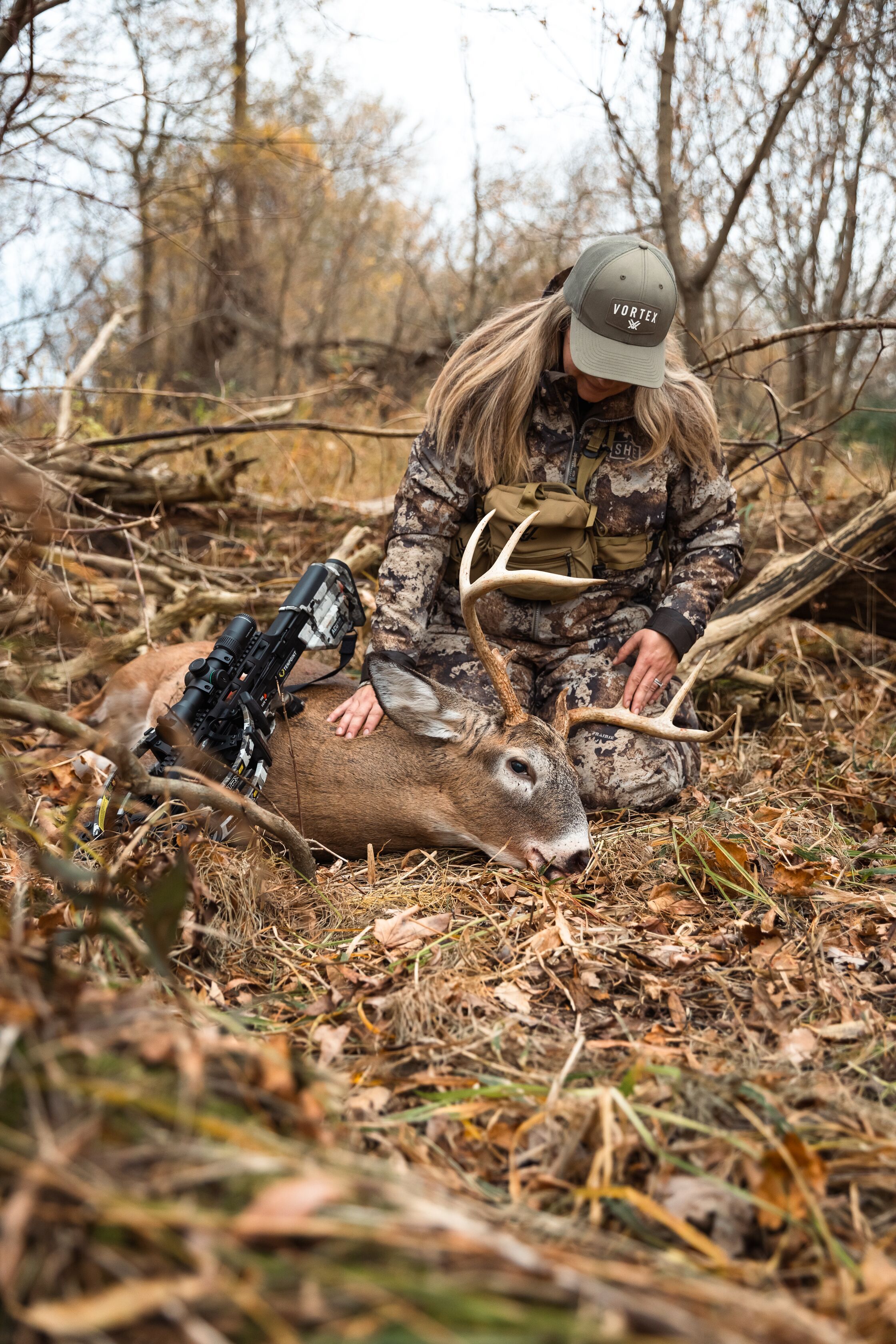 A female hunter leans over a buck deer on the ground after the hunt. 