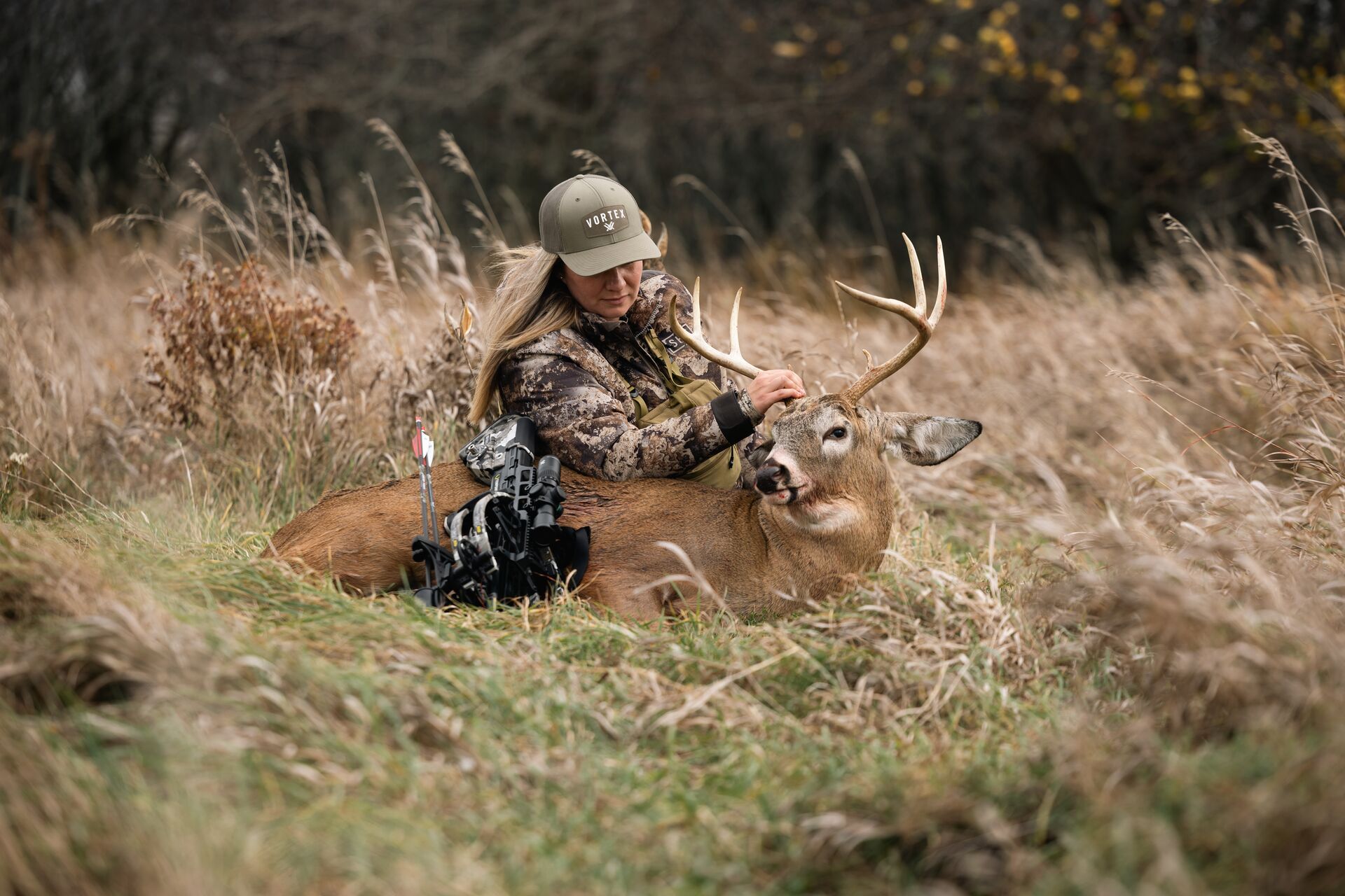 Female hunter poses with deer on the ground after hunt.