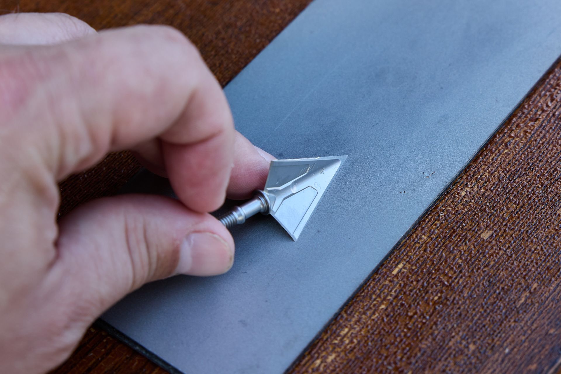 A hand holds a broadhead against a surface. 