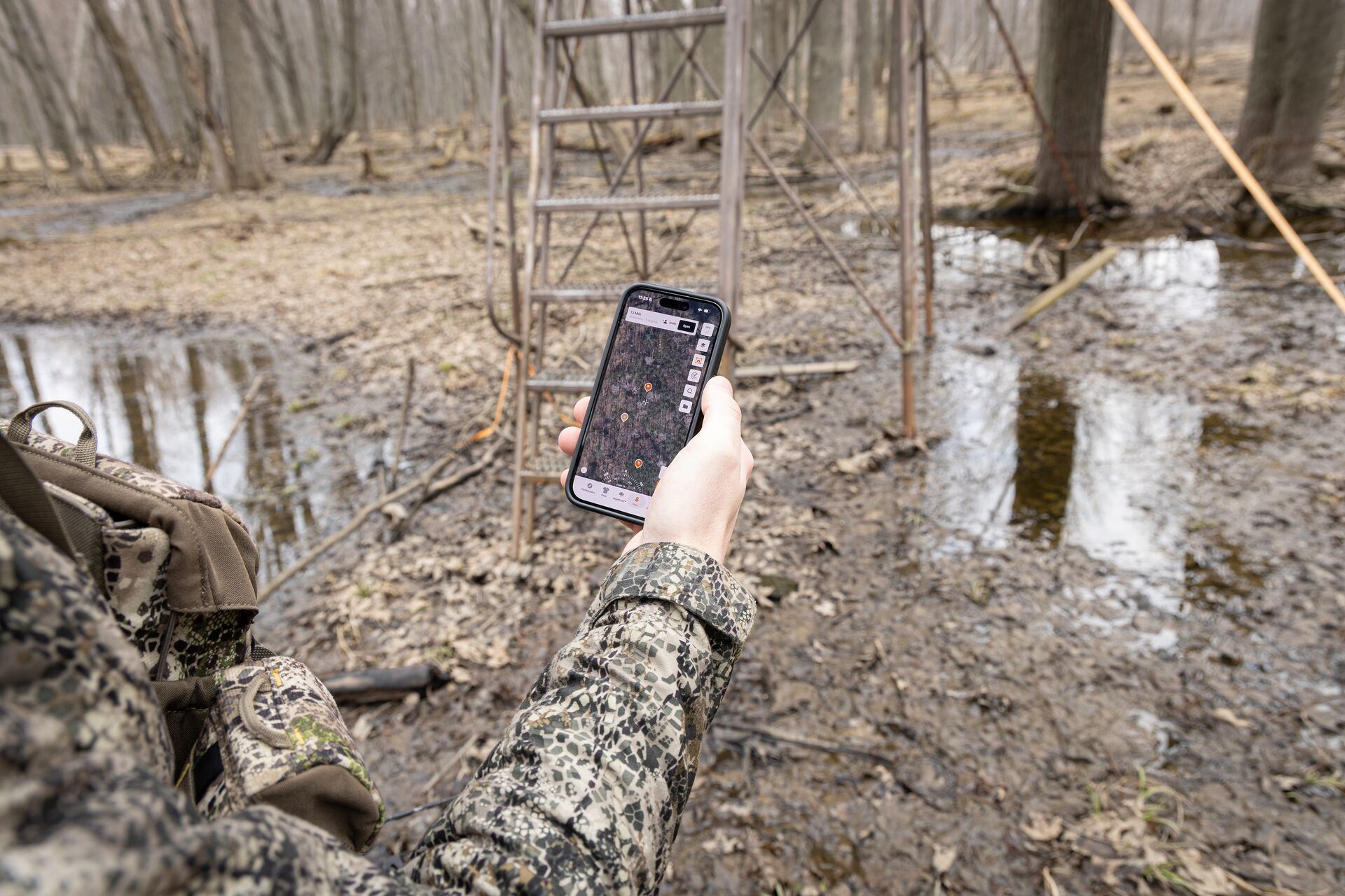 Hand holding phone showing HuntWise near stand, find property lines for hunting concept.