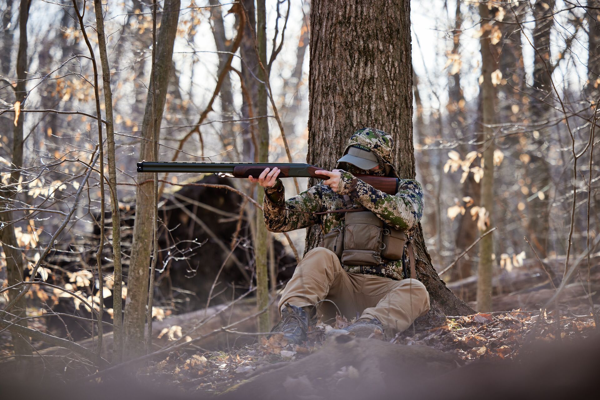 Hunter in the woods aims a shotgun for turkey hunt. 