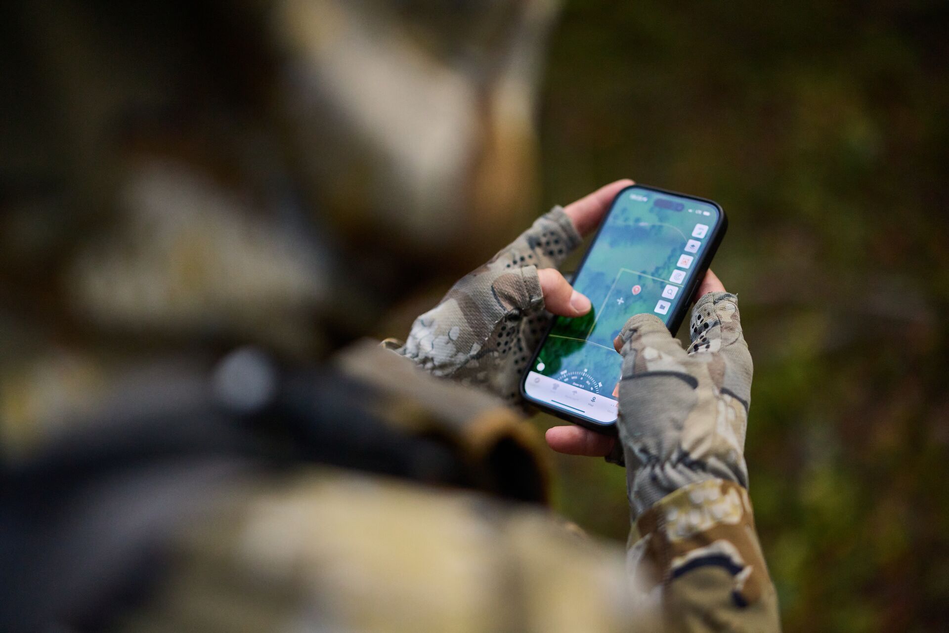 Hunter holds phone showing HuntWise terrain view, Wyoming elk hunt concept. 