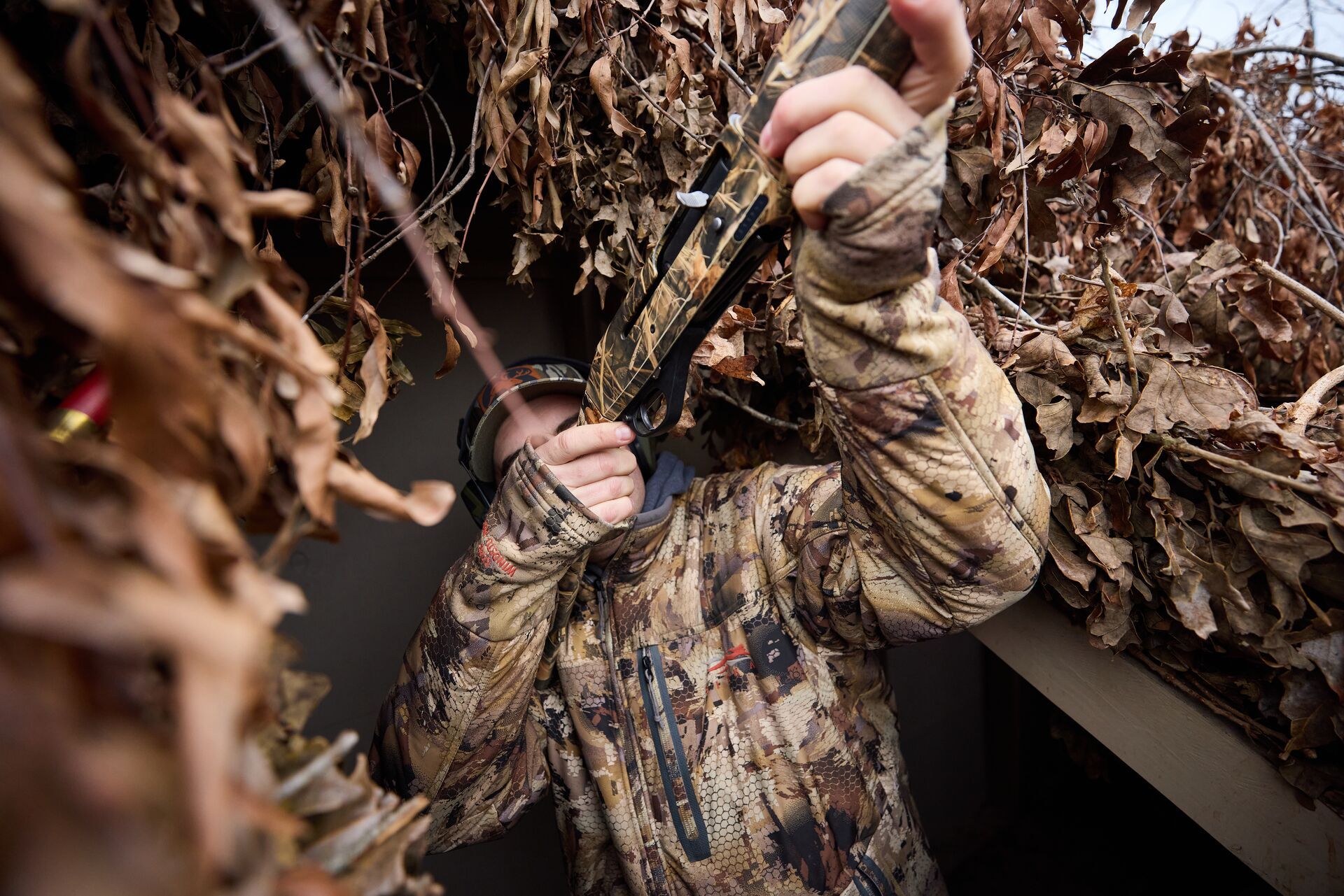 Hunter in camo in duck blind aims shotgun, building a duck pond concept. 