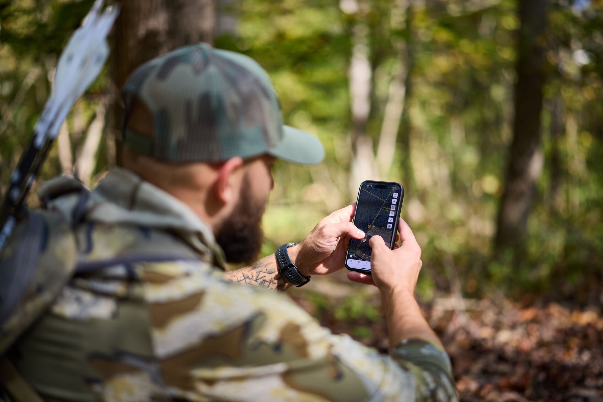 Hunter in the woods wearing camo using the HuntWise hunting app on a phone. 