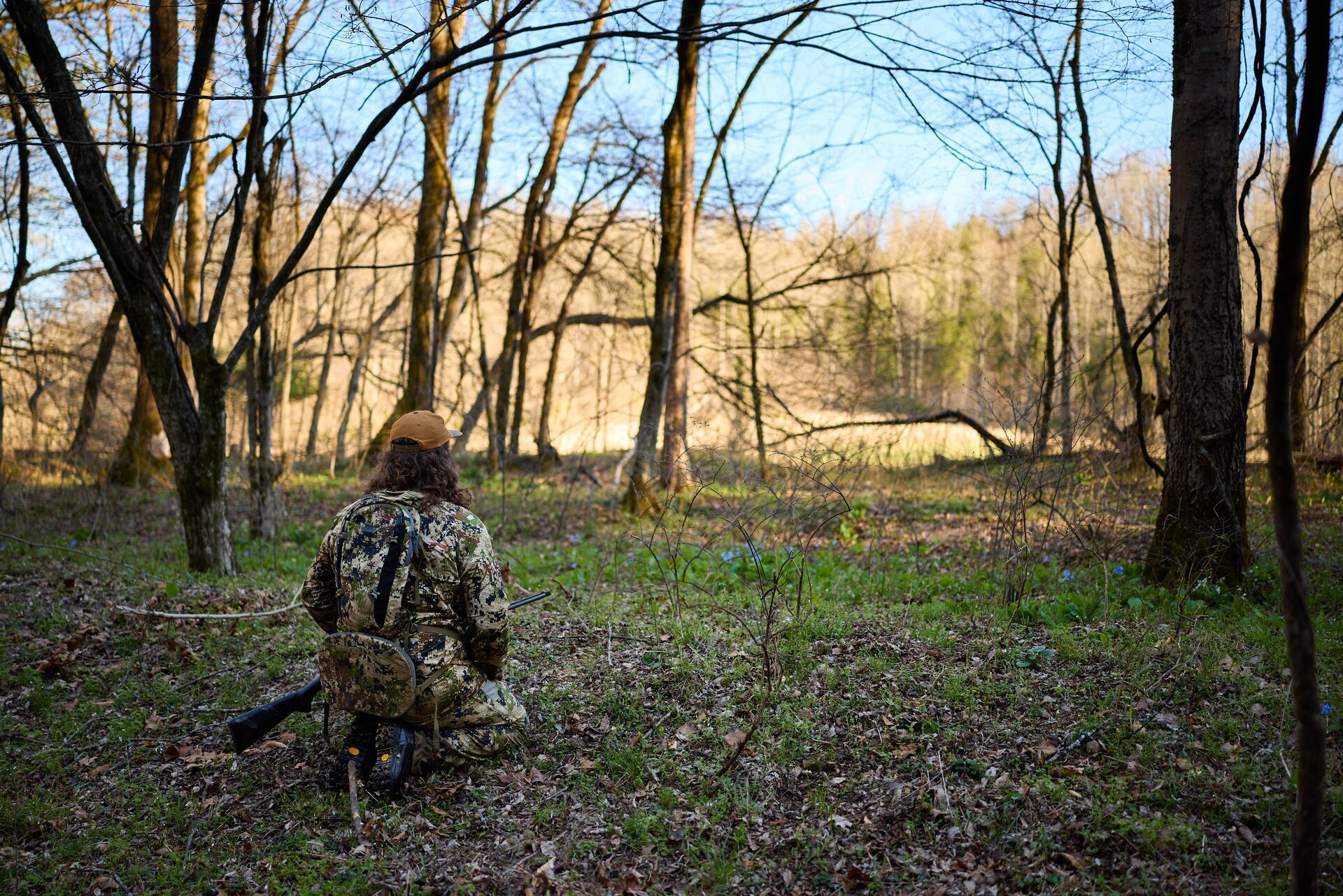 Hunter in camo kneels in the woods, how to make turkey sounds concept. 