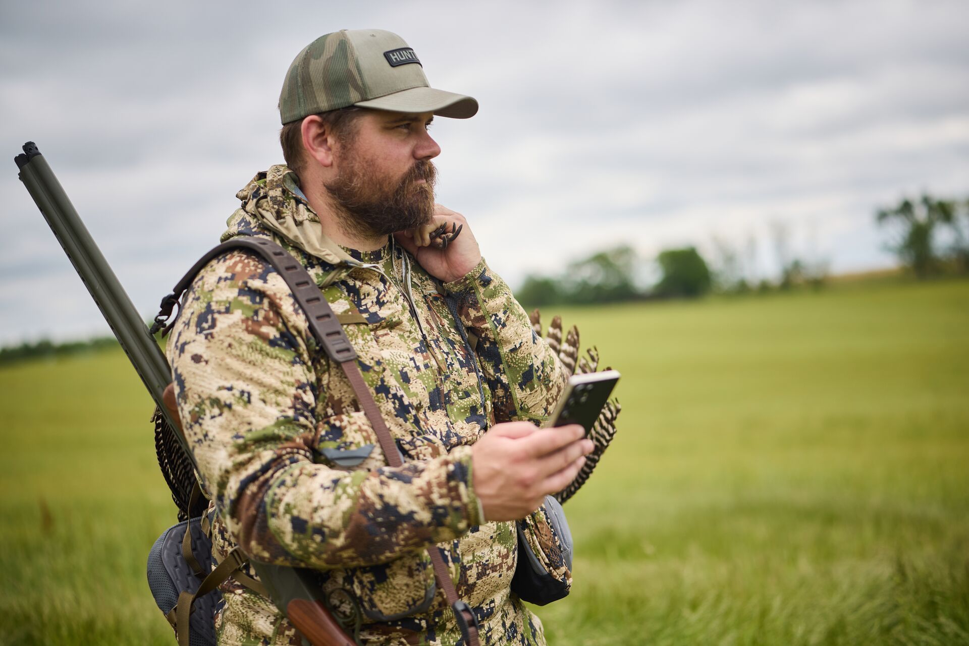 Hunter in camo with firearm and phone, HuntCast vs weather apps concept. 