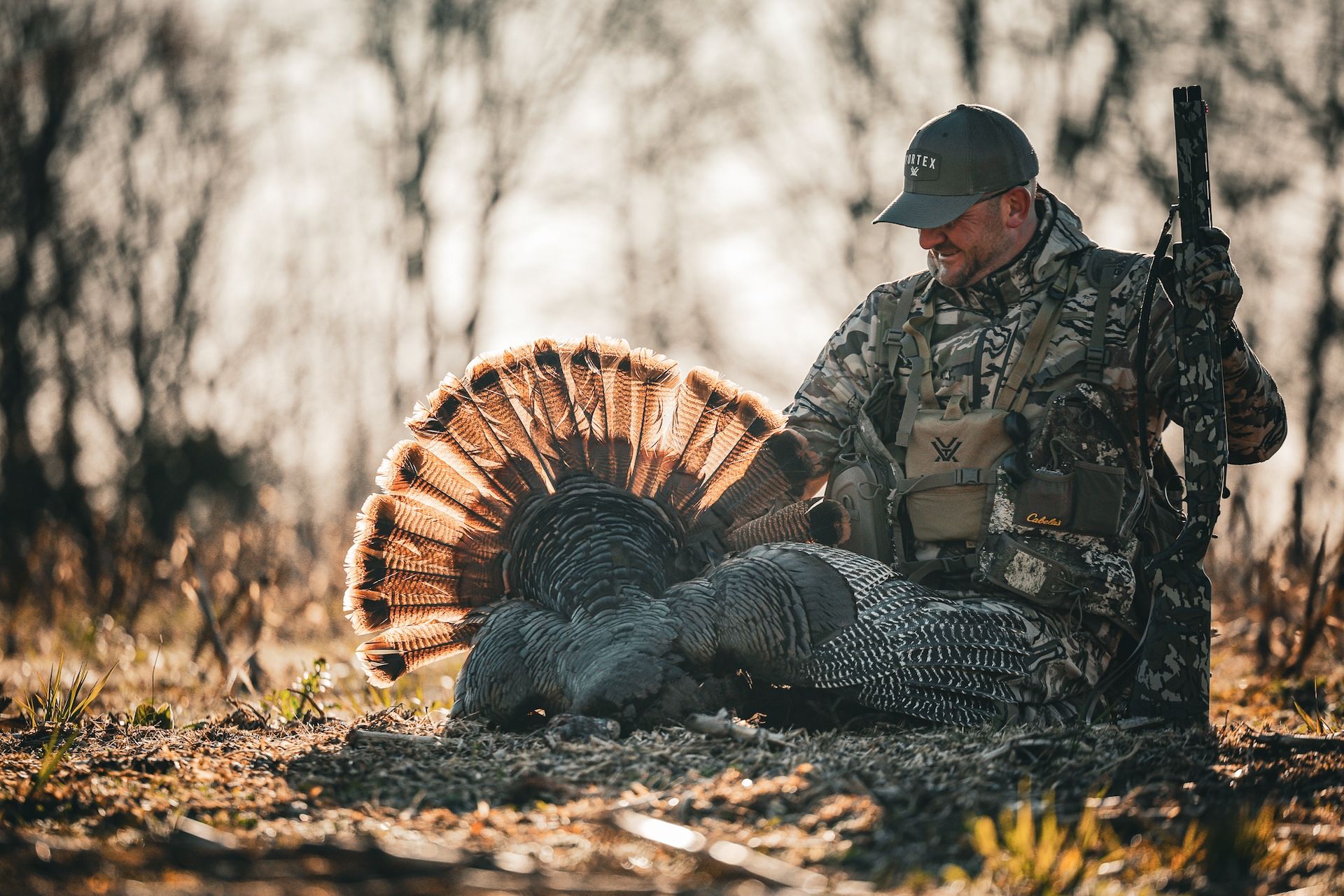 Hunter in camo with shotgun sits with turkey after hunt, South Dakota turkey hunting concept. 