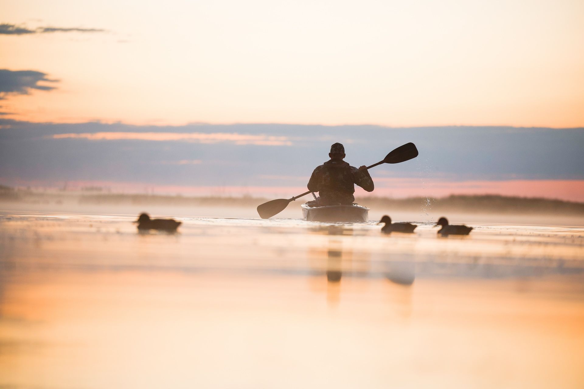 Hunter paddles canoe on water with decoys nearby for a waterfowl hunt. 