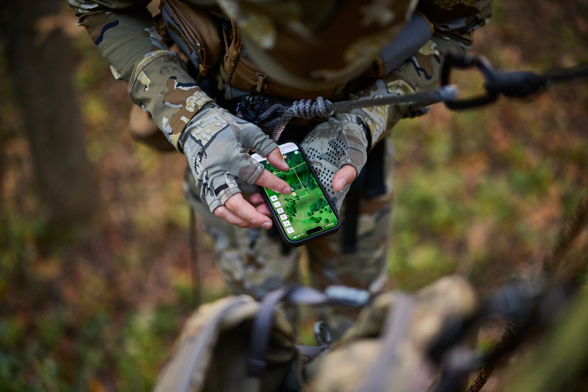 Hunter in tree saddle uses HuntWise on phone. 