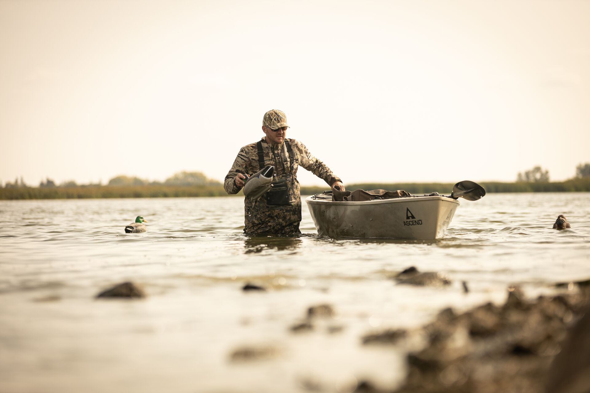 Hunter in waders in the water with canoe setting decoys, best duck hunting equipment concept. 