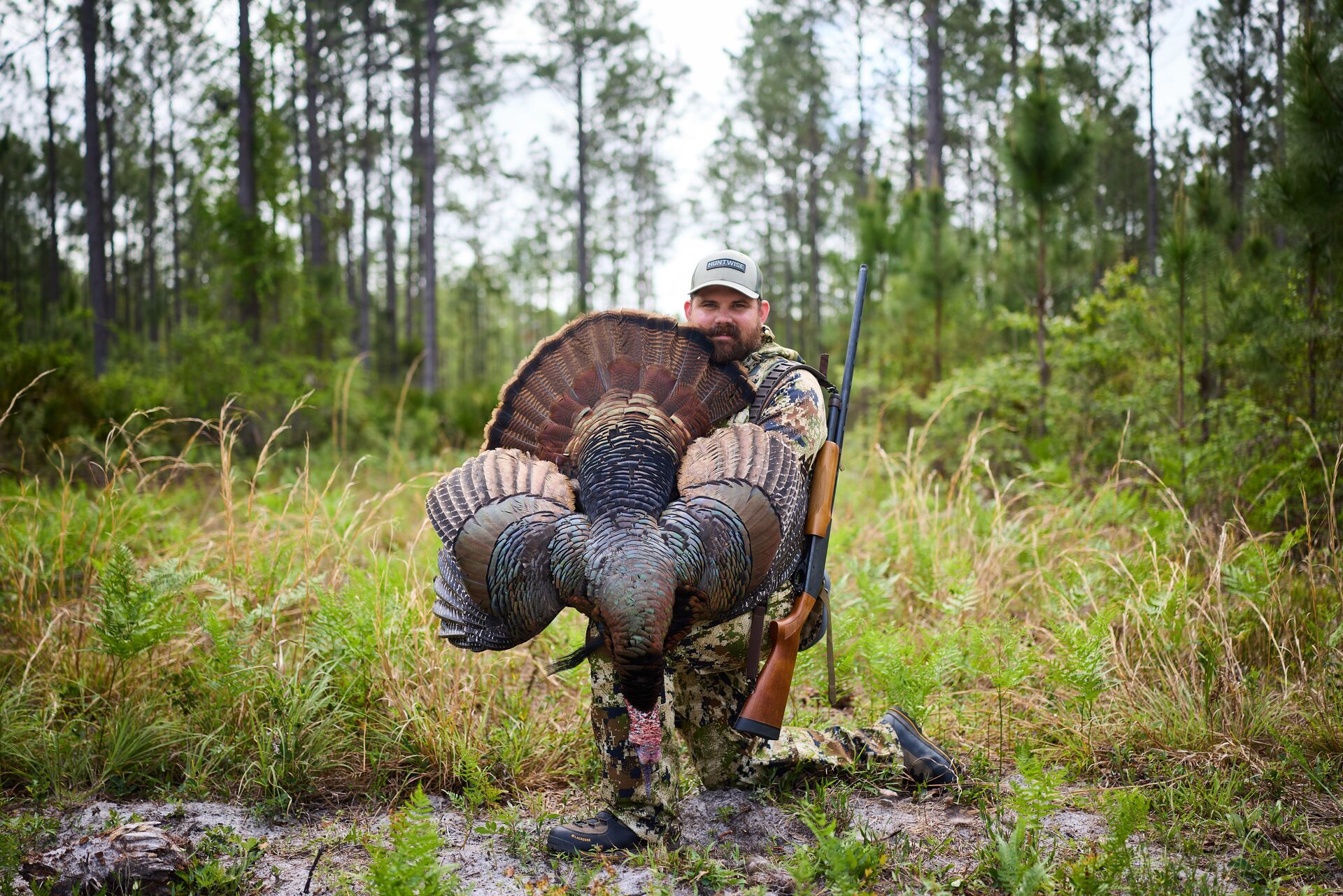 Hunter kneels with turkey after hunt, best caliber for turkey hunting concept. 
