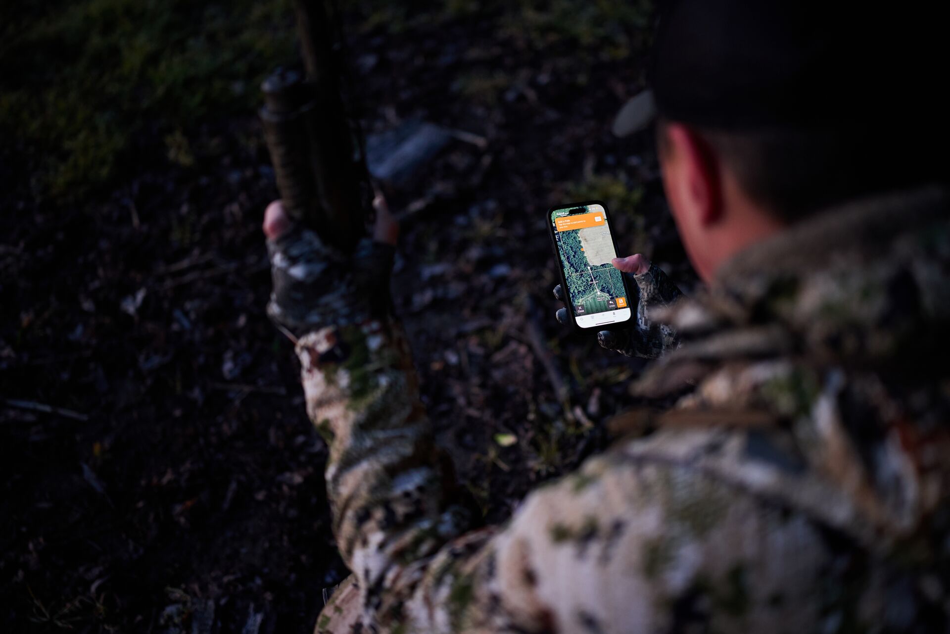 Hunter kneels in the woods using HuntWise maps on a phone.