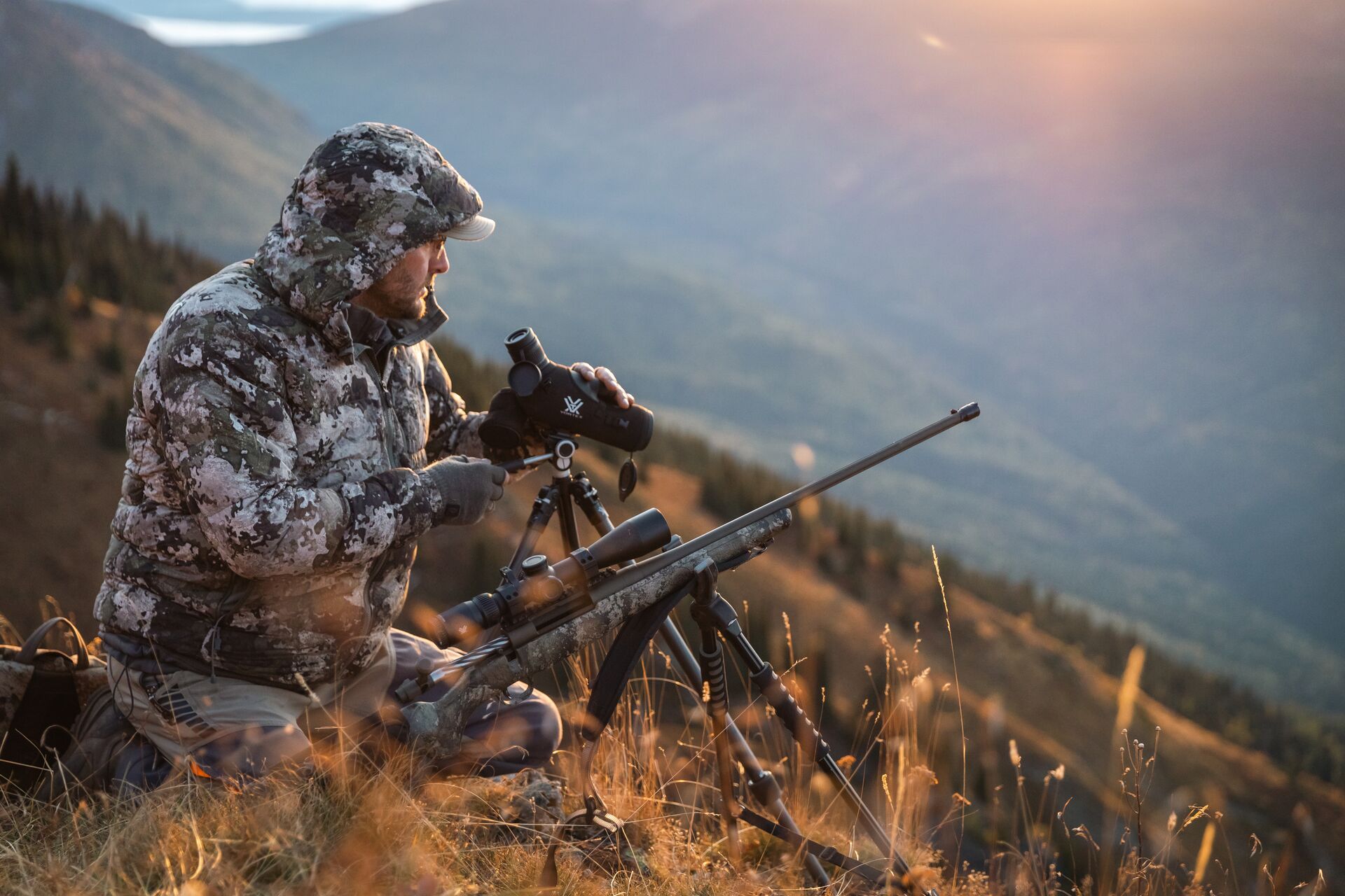 Hunter on hill with spotting scope and rifle, mule deer scouting tips concept. 
