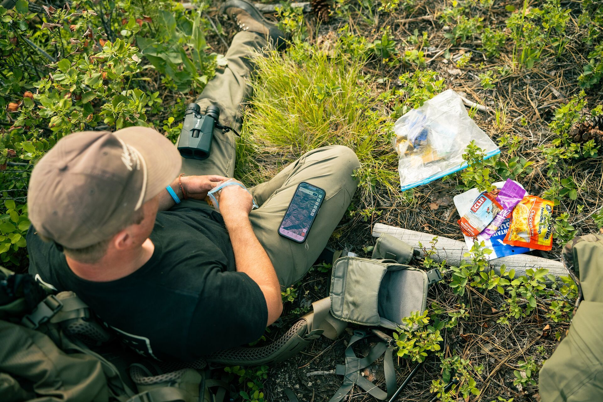 Hunter on the ground with gear and HuntWise on phone, escouting mule deer. 