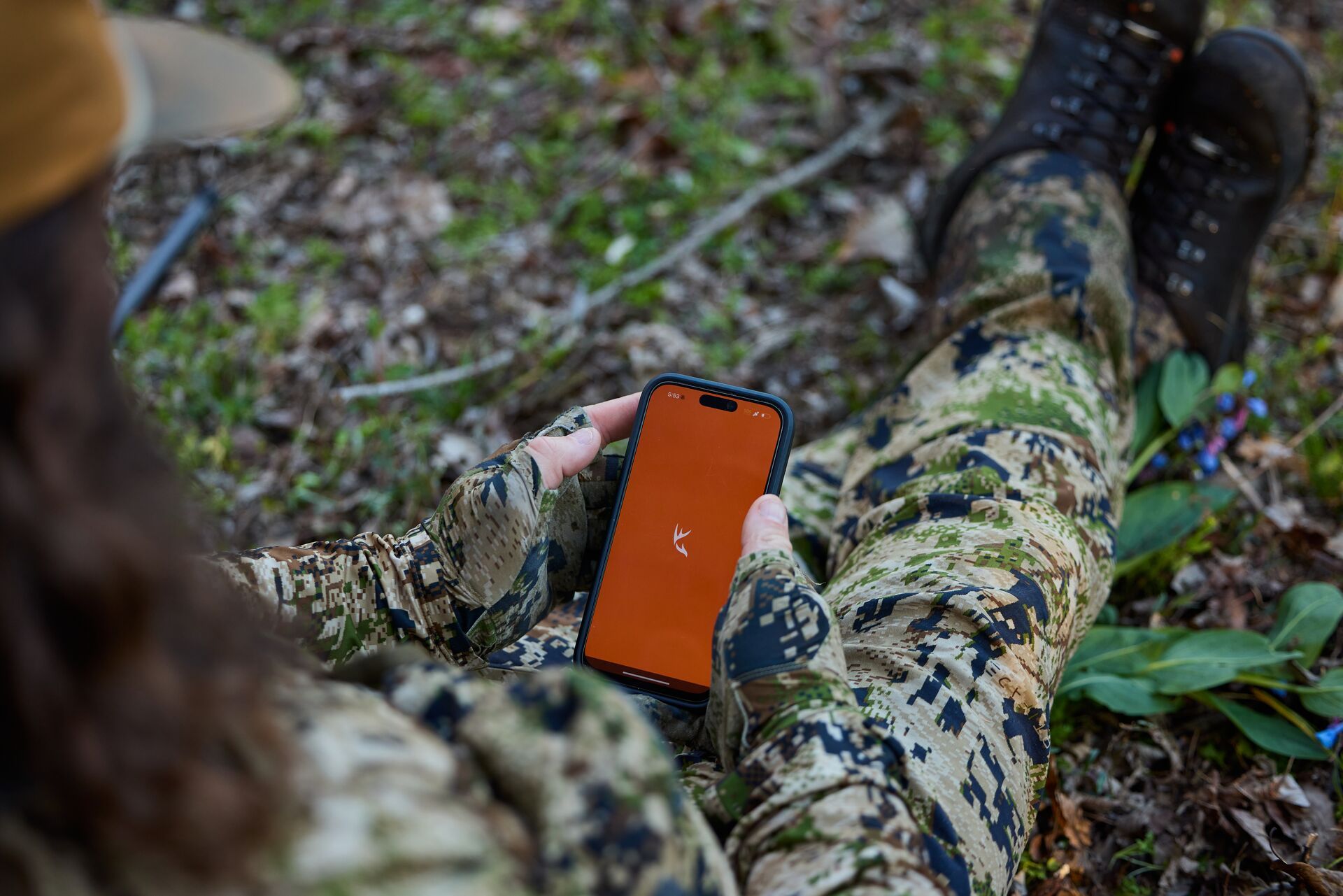 A hunter sits on the ground with the HuntWise app on a phone screen. 