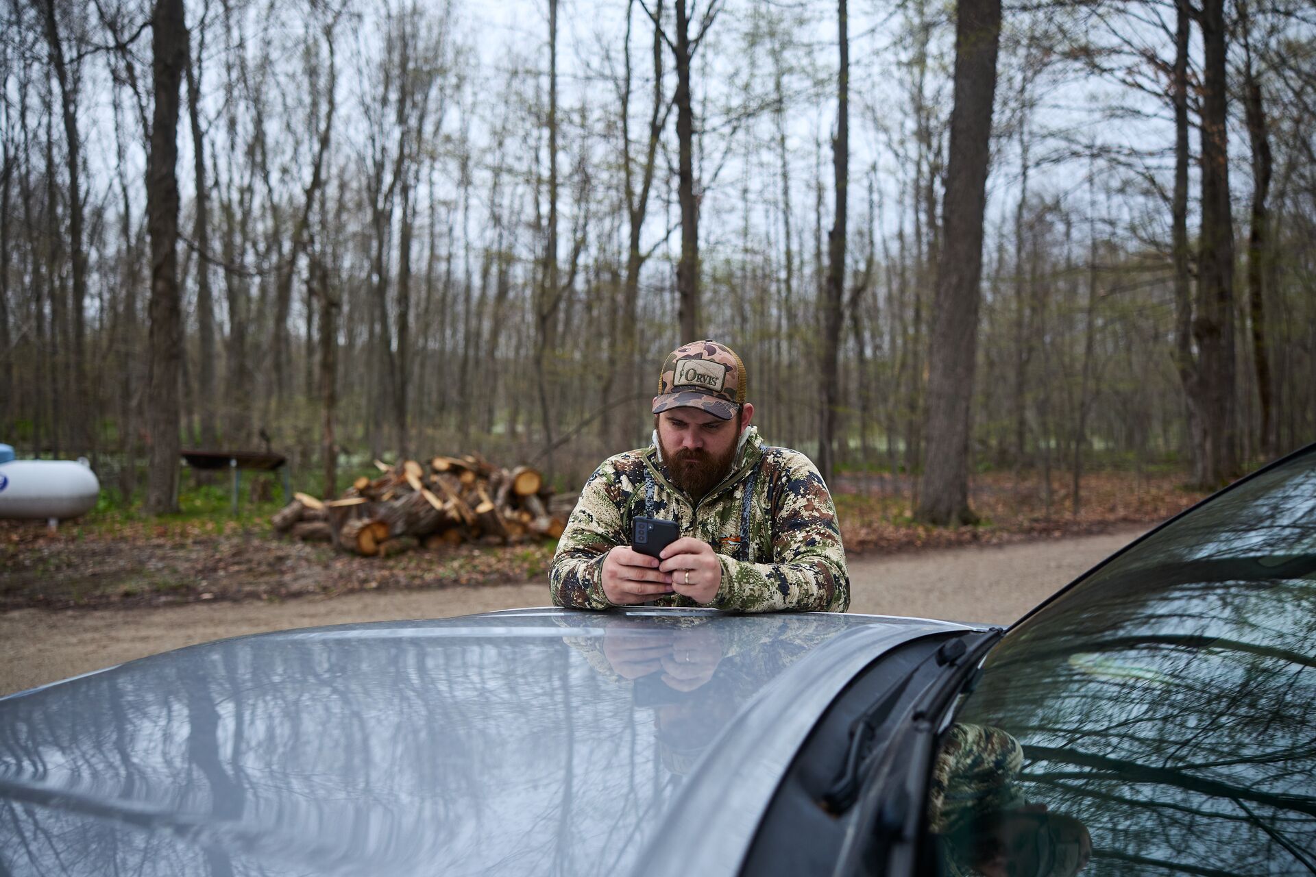 A hunter leans on a truck and looks at his phone, use the HuntWise hunting app to find wild game concept. 