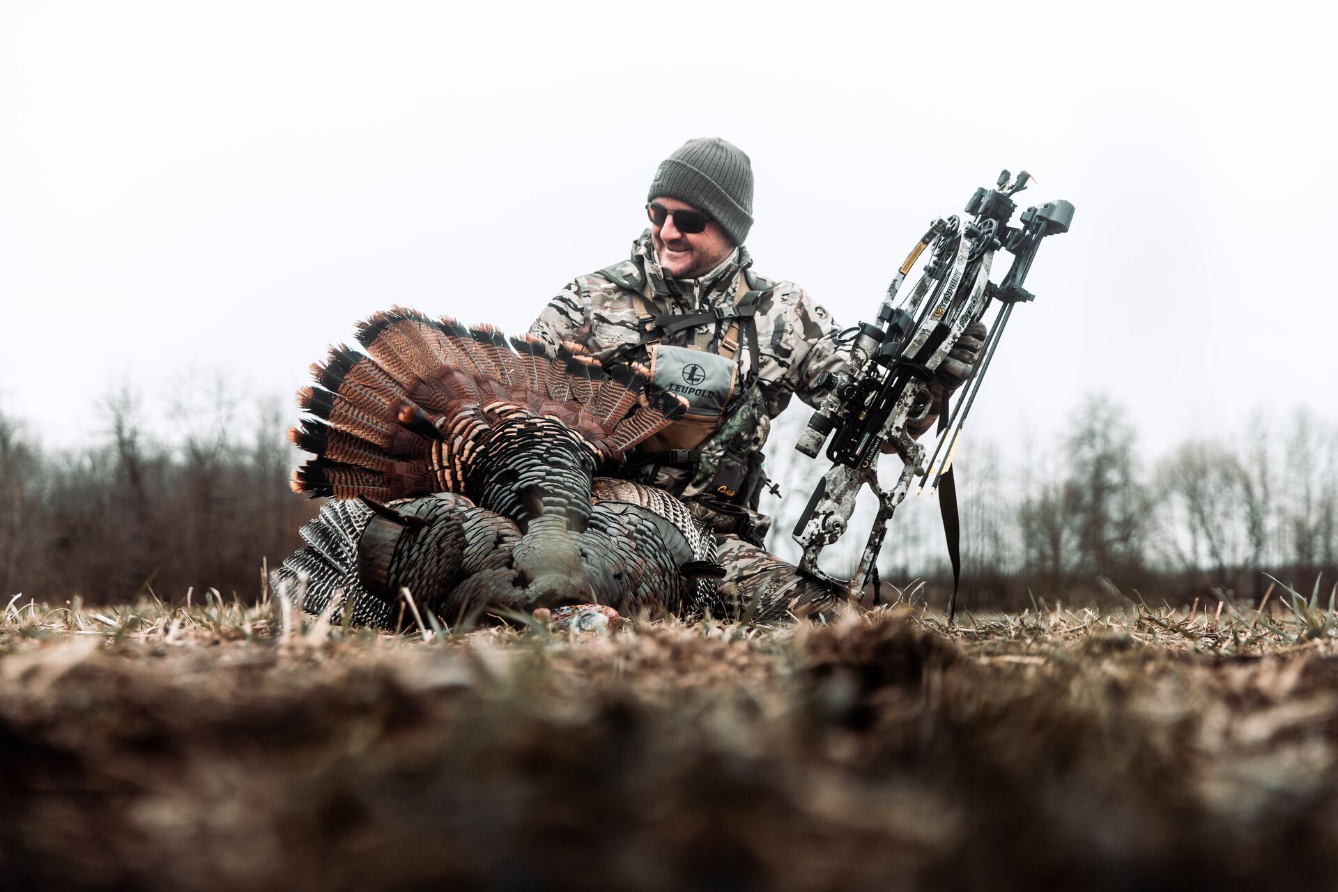 Hunter smiles with turkey and bow after hunt, best turkey hunting weather concept. 
