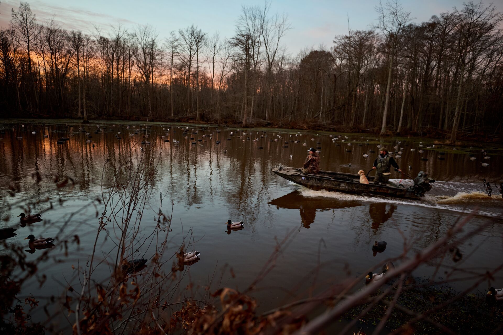 Hunters on boat surrounded by duck decoys on the water.