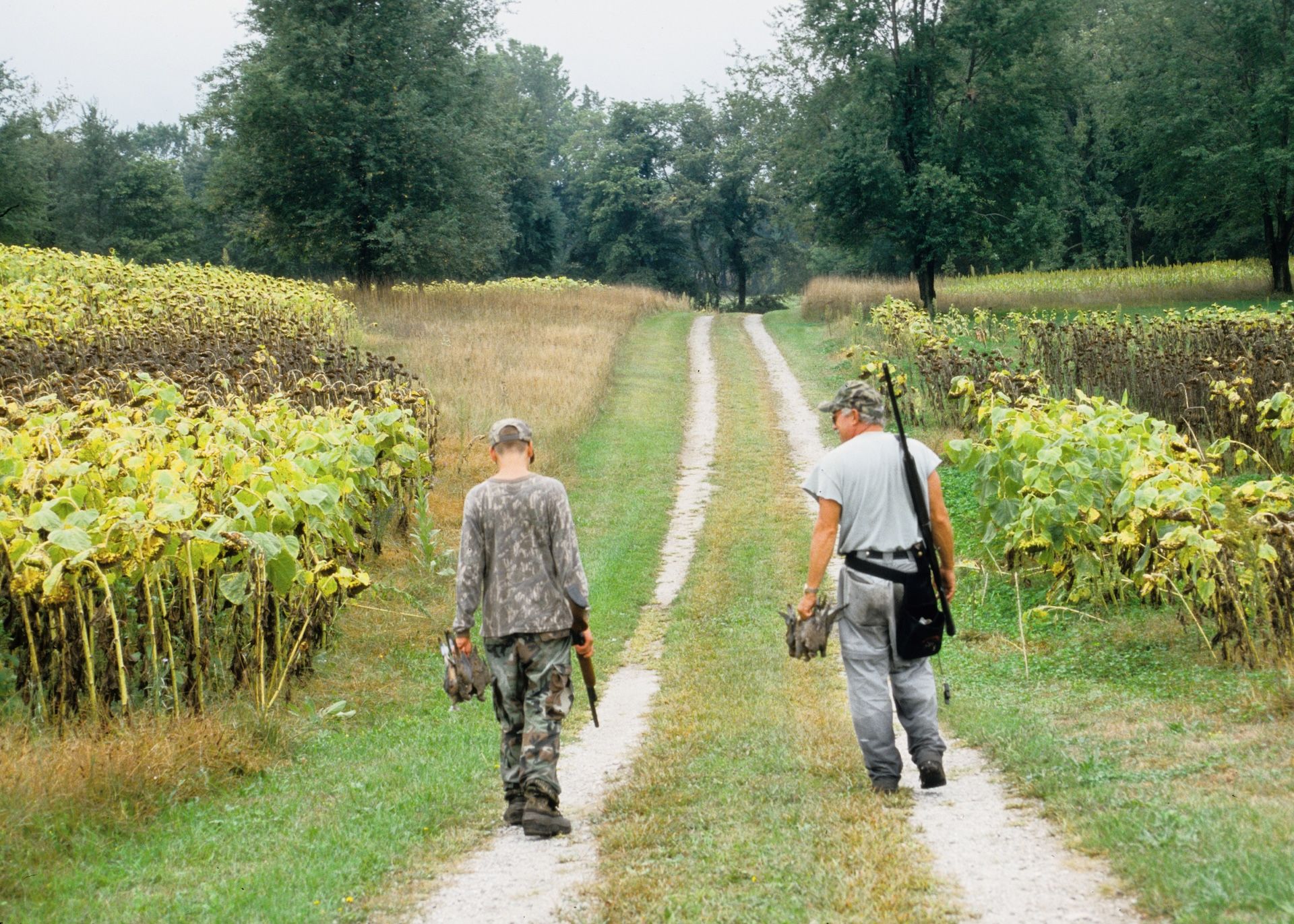 Two hunters walking with doves and shotguns after hunt.