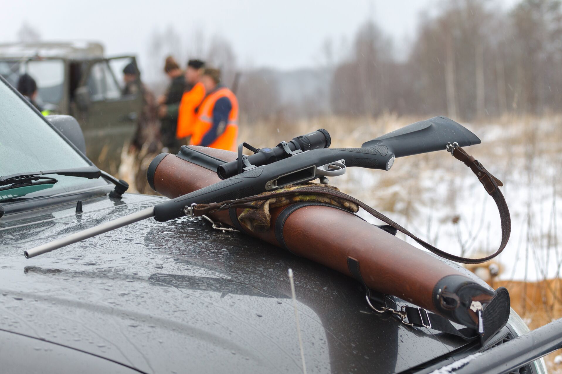 Hunting rifle on the hood of a truck with hunters in the back ground. 