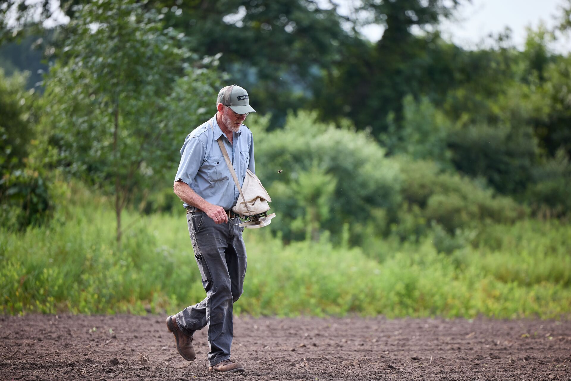 Man spreading plant seed by hand for spring food plot. 
