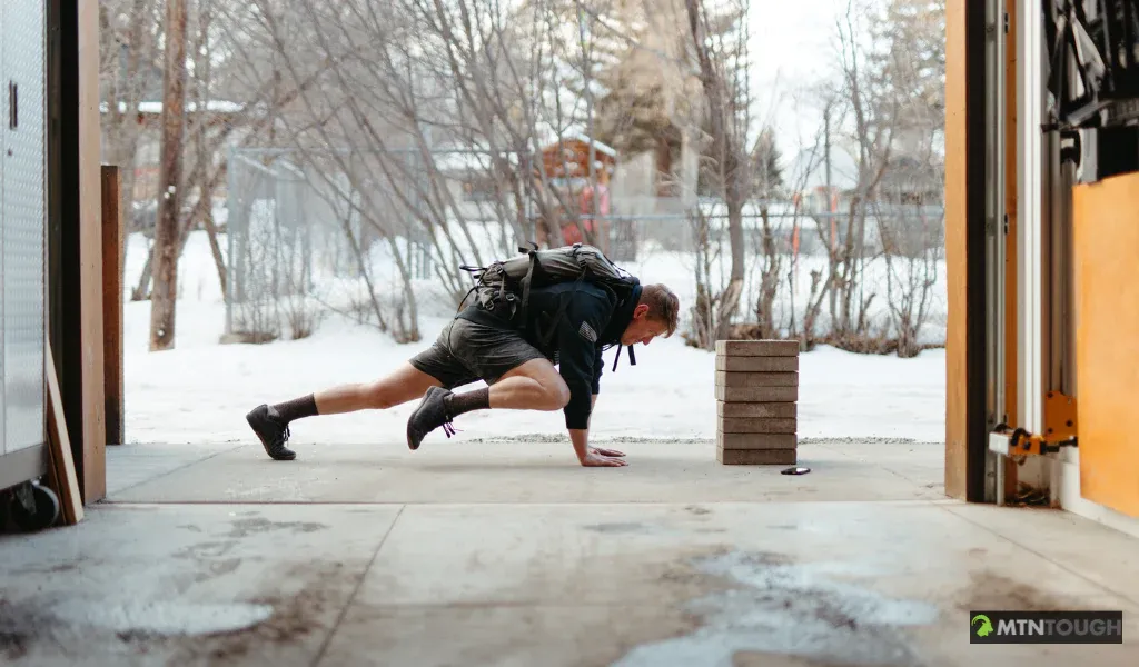 A man wearing a pack doing mountain climbers, hunting workouts concept. 