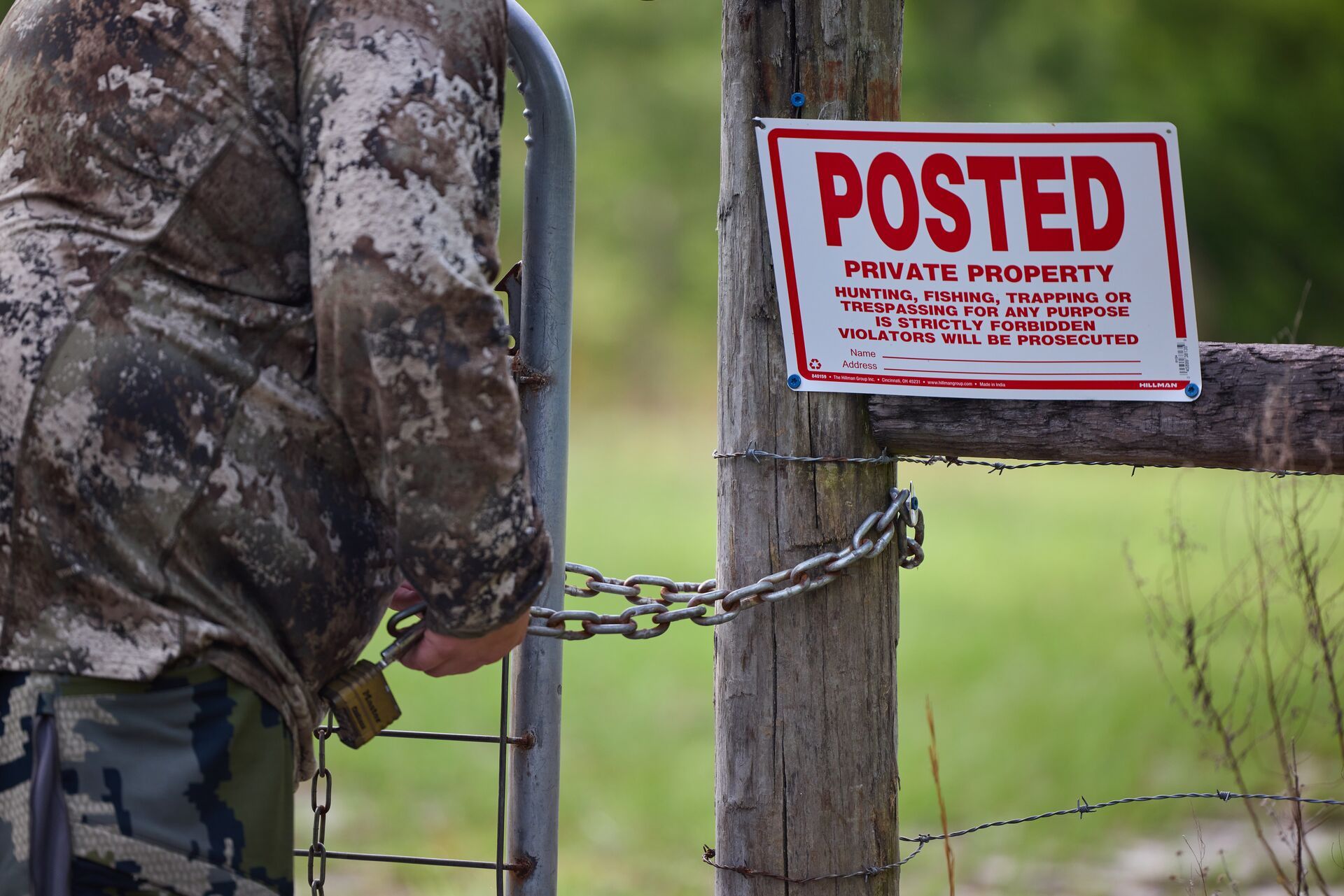 Hunter removing chain from fence near private property sign. 