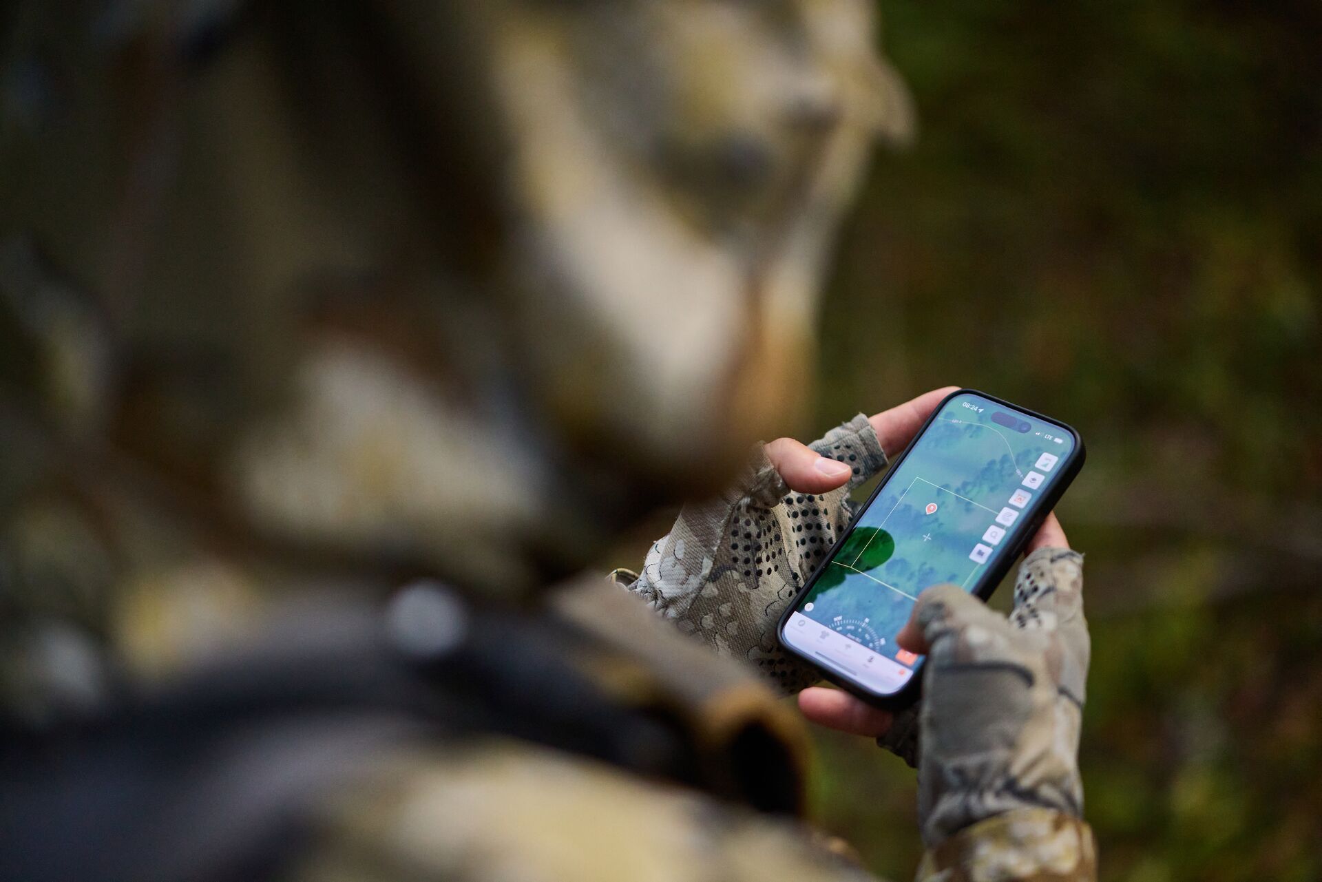 Over the shoulder view of hunter looking at HuntWise on phone, use a hunting app concept.