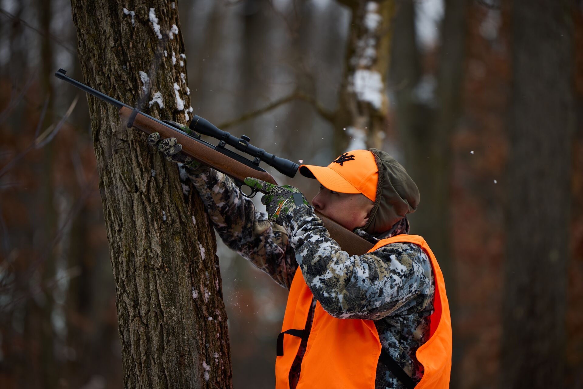 A hunter in blaze orange aims a rifle, squirrel hunting gear concept. 