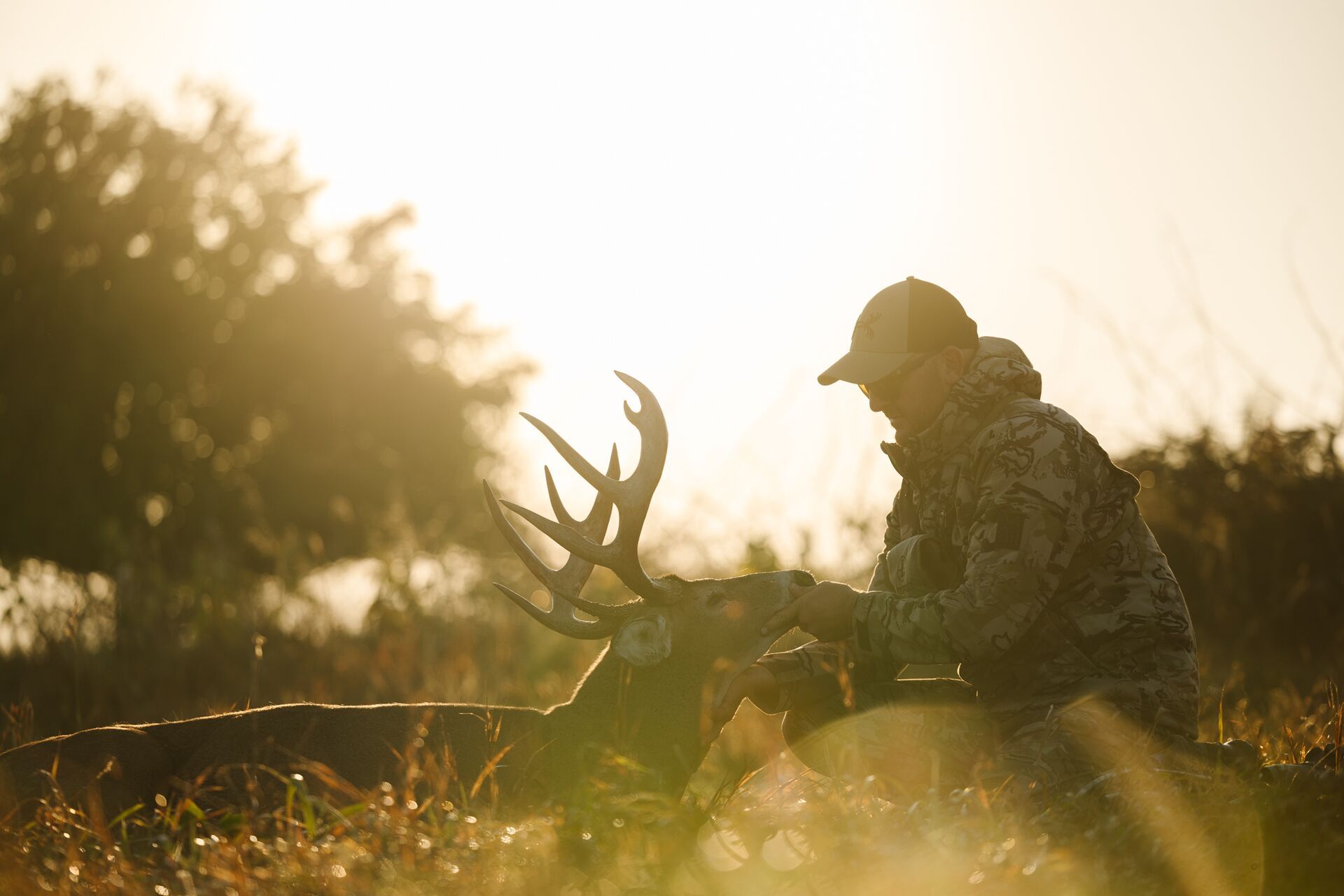 Sun behind hunter on the ground looking at deer after hunt.