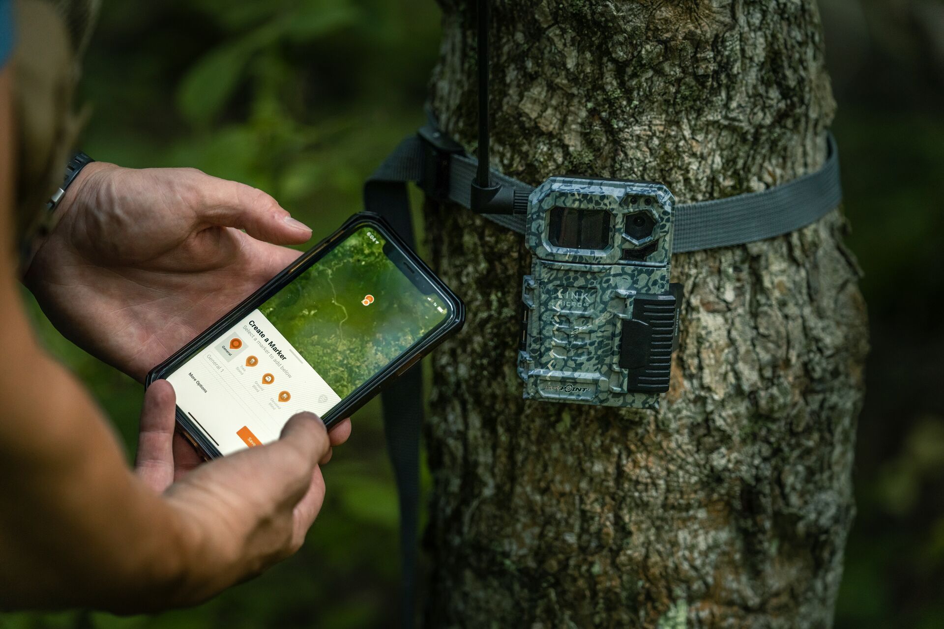 A trail cam and someone holding a phone showing the HuntWise app best hunting gifts for moms concept. 