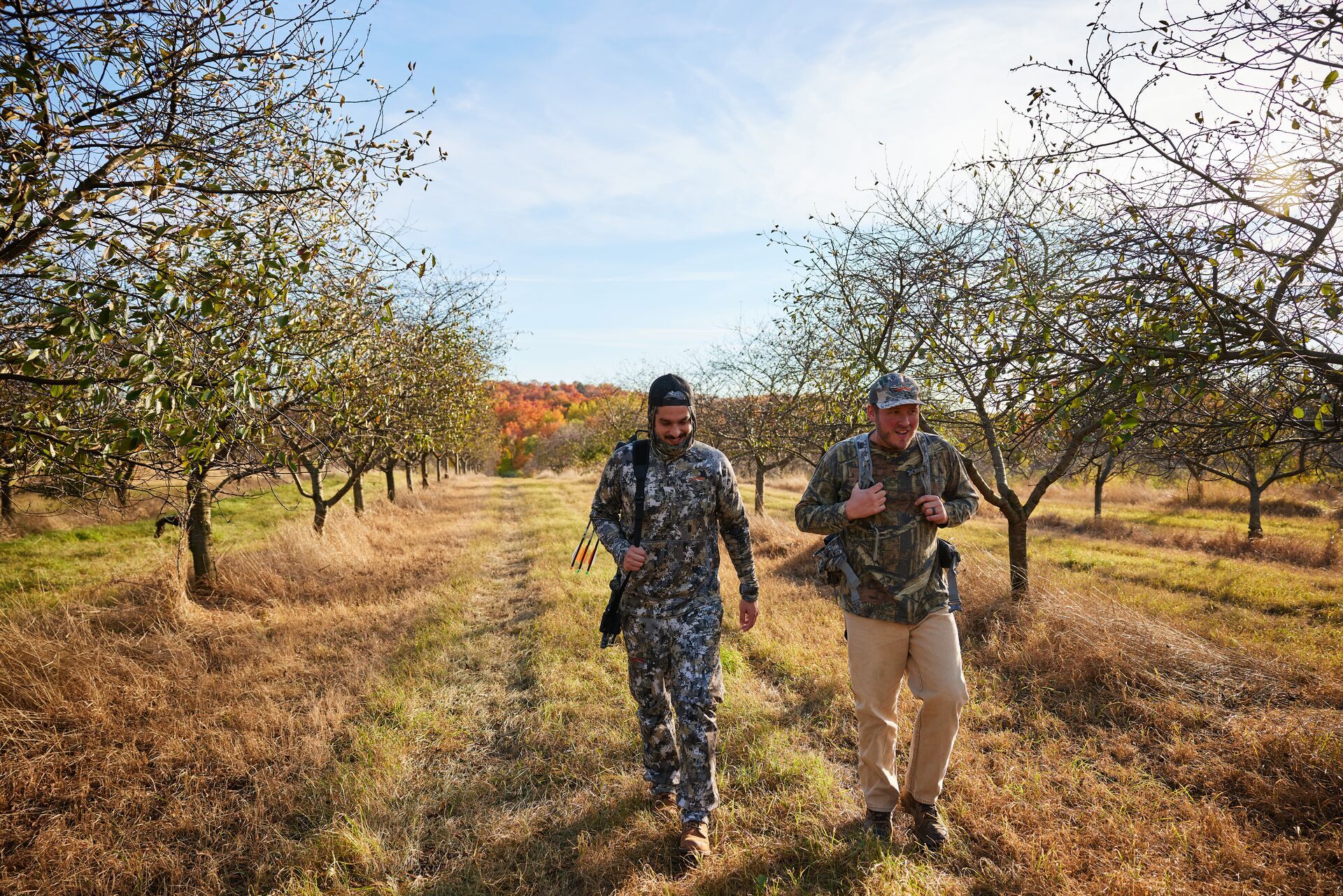 Two hunters in camo walk a trail in the woods. 