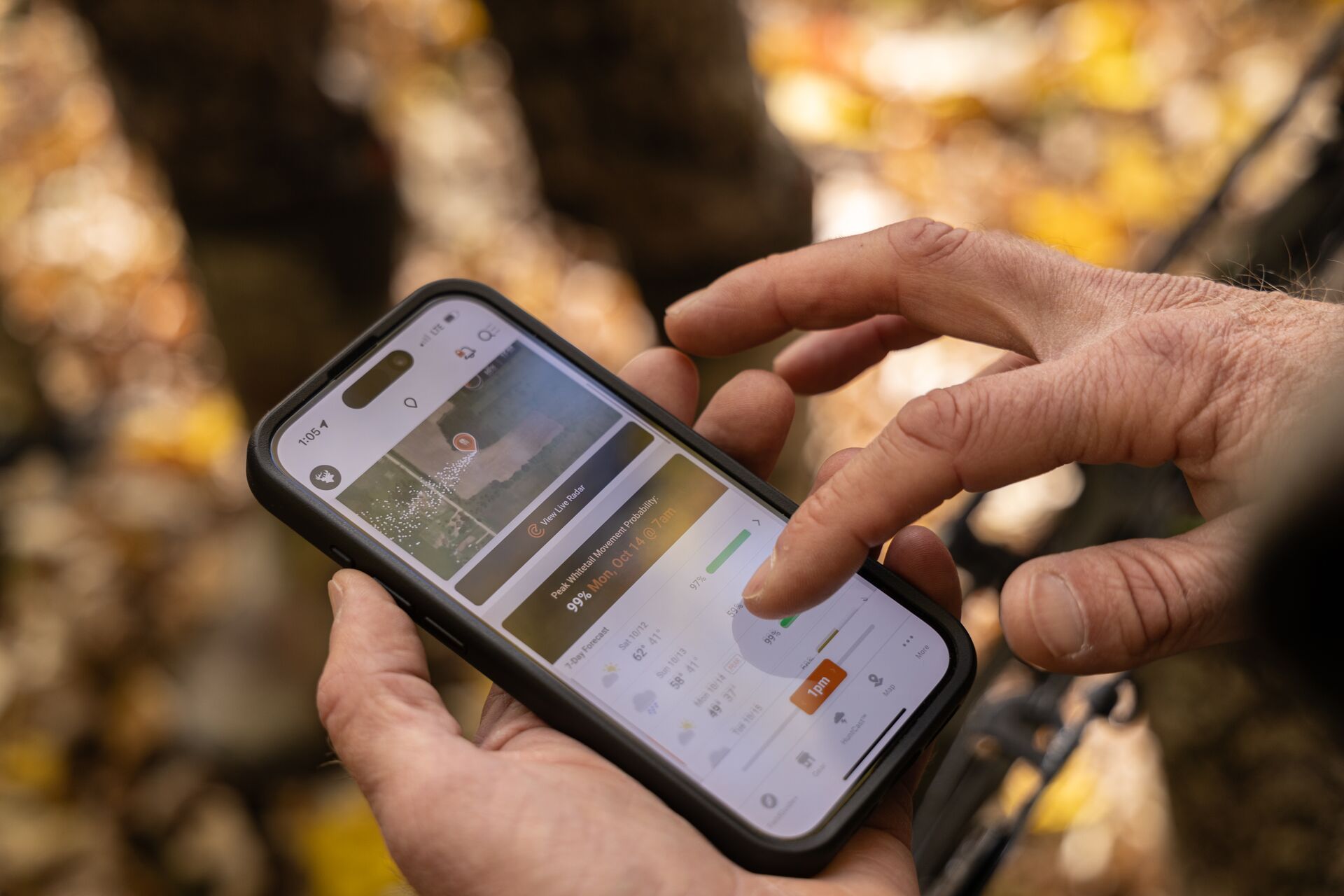 Close-up of hands holding a phone and using the HuntWise hunting app. 